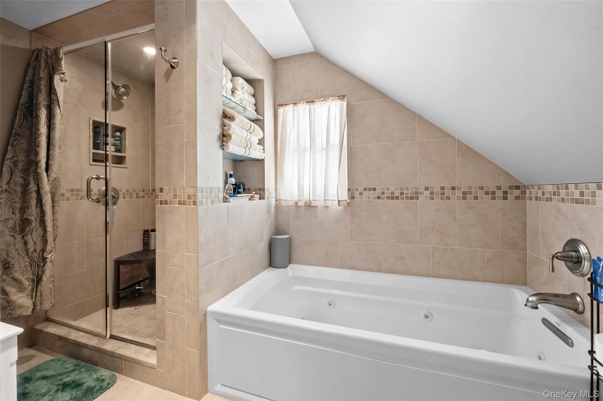 Tiled bathroom featuring a glass-enclosed shower, a built-in storage niche with glass shelving, and a separate jetted tub Tiled bathroom featuring a glass-enclosed shower, a built-in storage niche with glass shelving, and a separate jetted tub