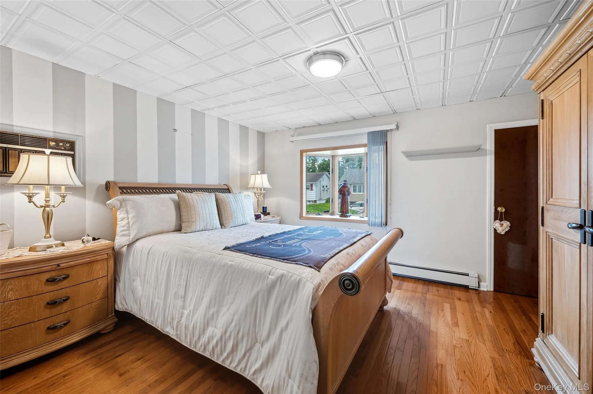 Bedroom featuring rich wood-finish flooring, a textured white ceiling, and a prominent window Bedroom featuring rich wood-finish flooring, a textured white ceiling, and a prominent window