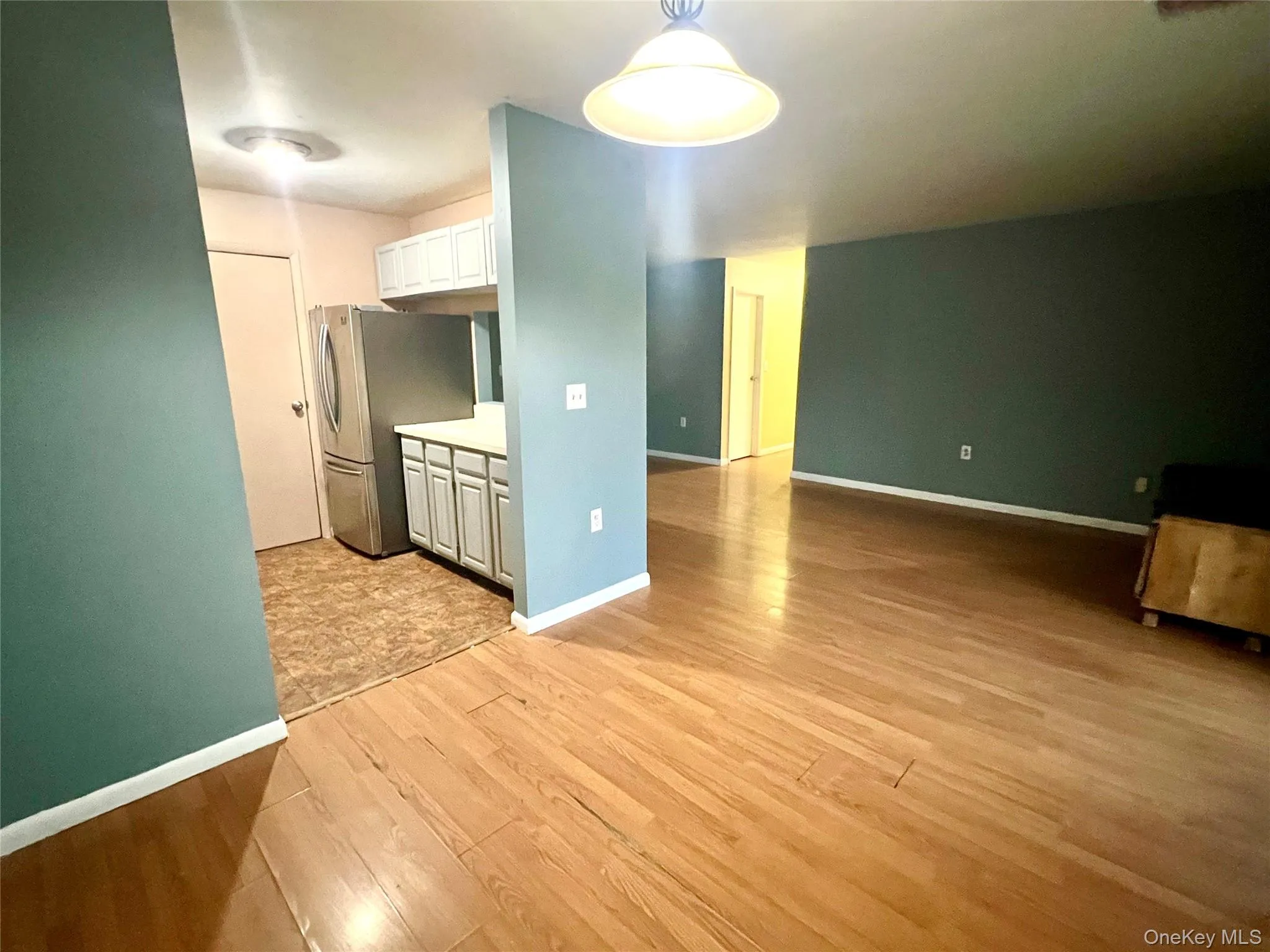 Kitchen with light countertops, white cabinets, light wood-style flooring, freestanding refrigerator, and hanging light fixtures Kitchen with light countertops, white cabinets, light wood-style flooring, freestanding refrigerator, and hanging light fixtures