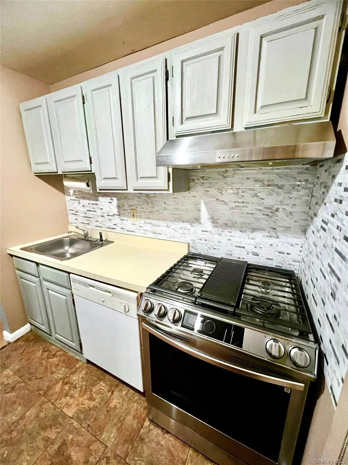 Kitchen featuring stainless steel range with gas cooktop, backsplash, light countertops, white dishwasher, and under cabinet range hood Kitchen featuring stainless steel range with gas cooktop, backsplash, light countertops, white dishwasher, and under cabinet range hood