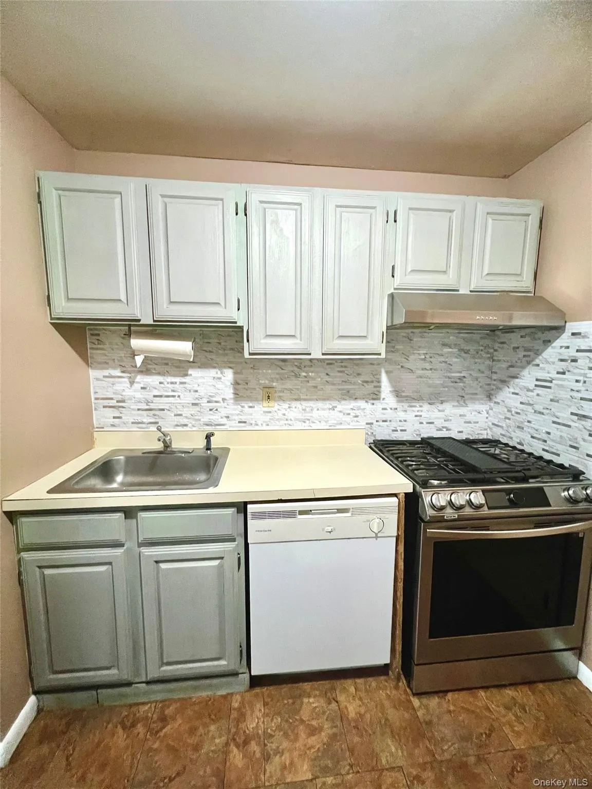 Kitchen with stainless steel range with gas cooktop, light countertops, white dishwasher, decorative backsplash, and under cabinet range hood Kitchen with stainless steel range with gas cooktop, light countertops, white dishwasher, decorative backsplash, and under cabinet range hood