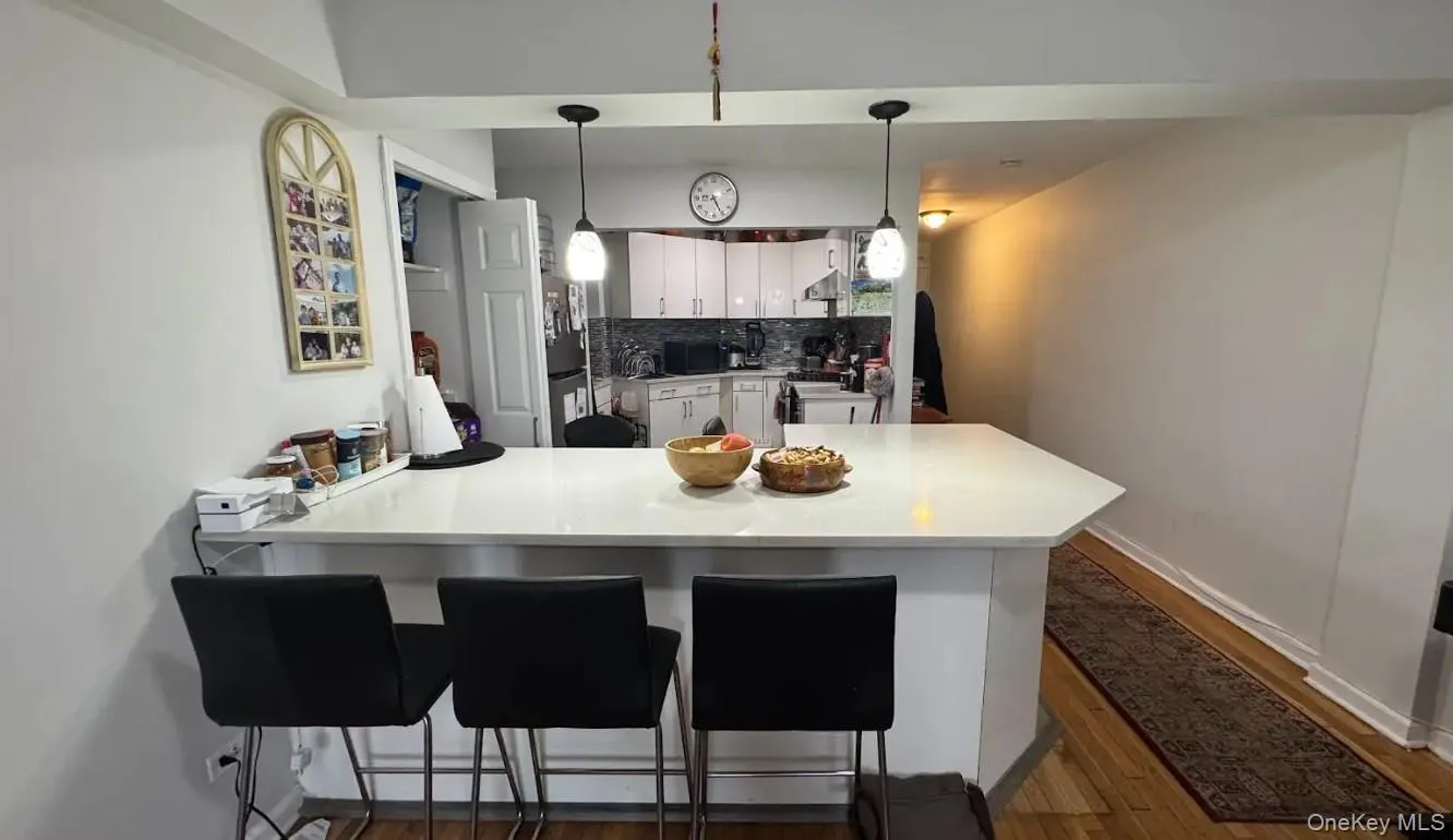 Kitchen featuring a peninsula, white cabinetry, tasteful backsplash, a breakfast bar area, and dark wood-style floors Kitchen featuring a peninsula, white cabinetry, tasteful backsplash, a breakfast bar area, and dark wood-style floors