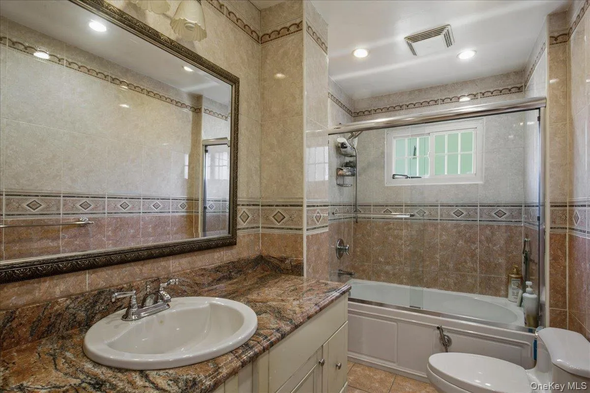 Hall bathroom featuring a built-in tub with glass enclosure, white framed window, and recessed lighting Hall bathroom featuring a built-in tub with glass enclosure, white framed window, and recessed lighting