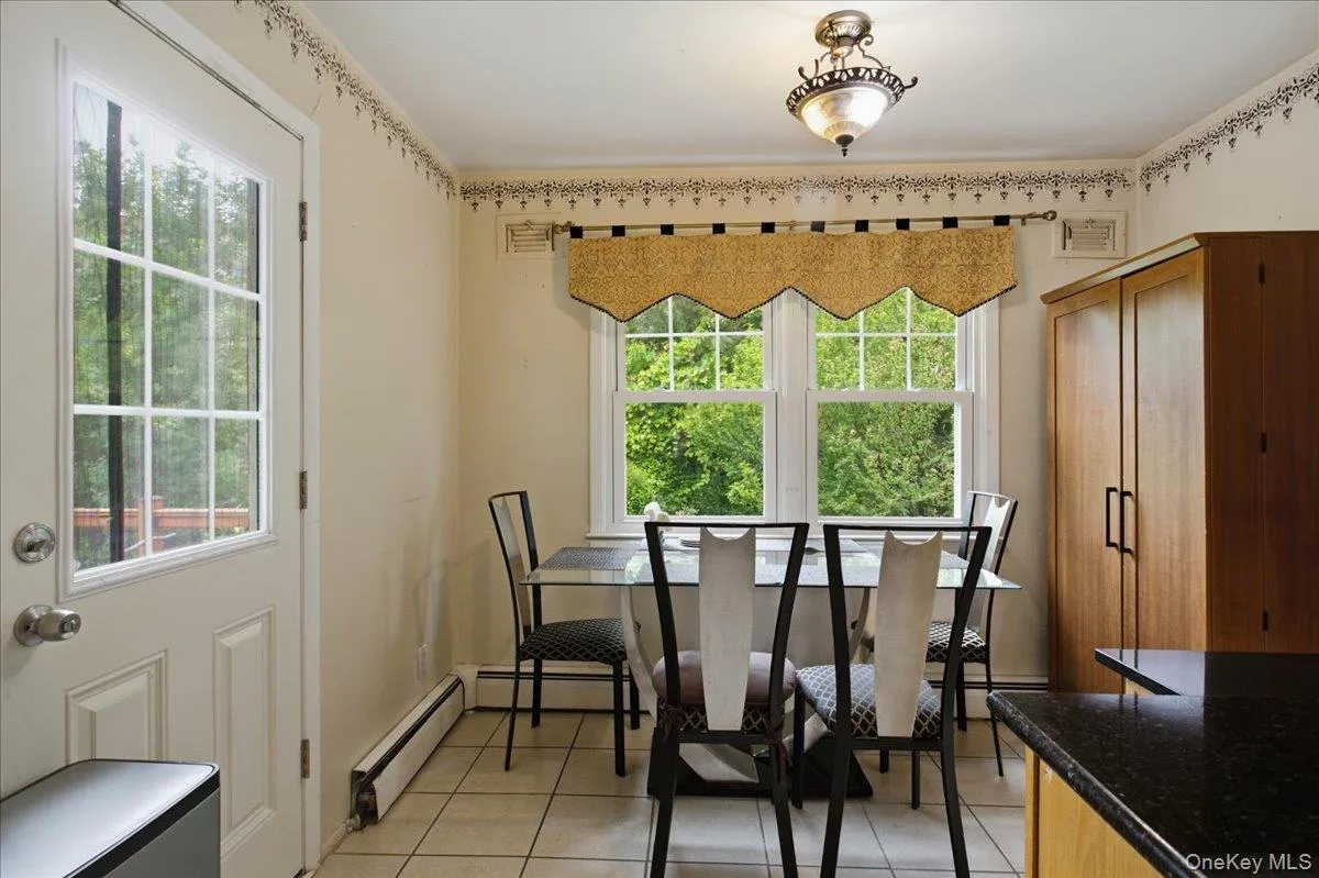Kitchen dining area featuring a glass-paned door, double windows, tiled flooring, built-in baseboard heating, and a flush-mount ceiling light fixture Kitchen dining area featuring a glass-paned door, double windows, tiled flooring, built-in baseboard heating, and a flush-mount ceiling light fixture