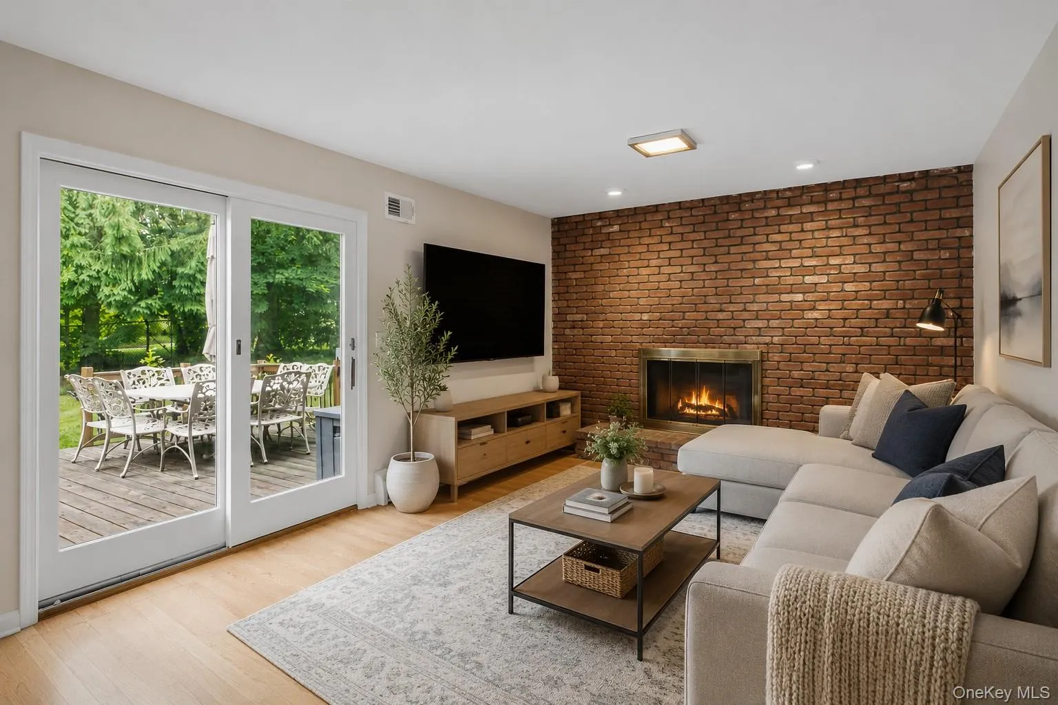 Brick accent wall with a fireplace, wood-finish flooring, recessed lighting, and sliding glass doors opening to an outdoor deck Brick accent wall with a fireplace, wood-finish flooring, recessed lighting, and sliding glass doors opening to an outdoor deck