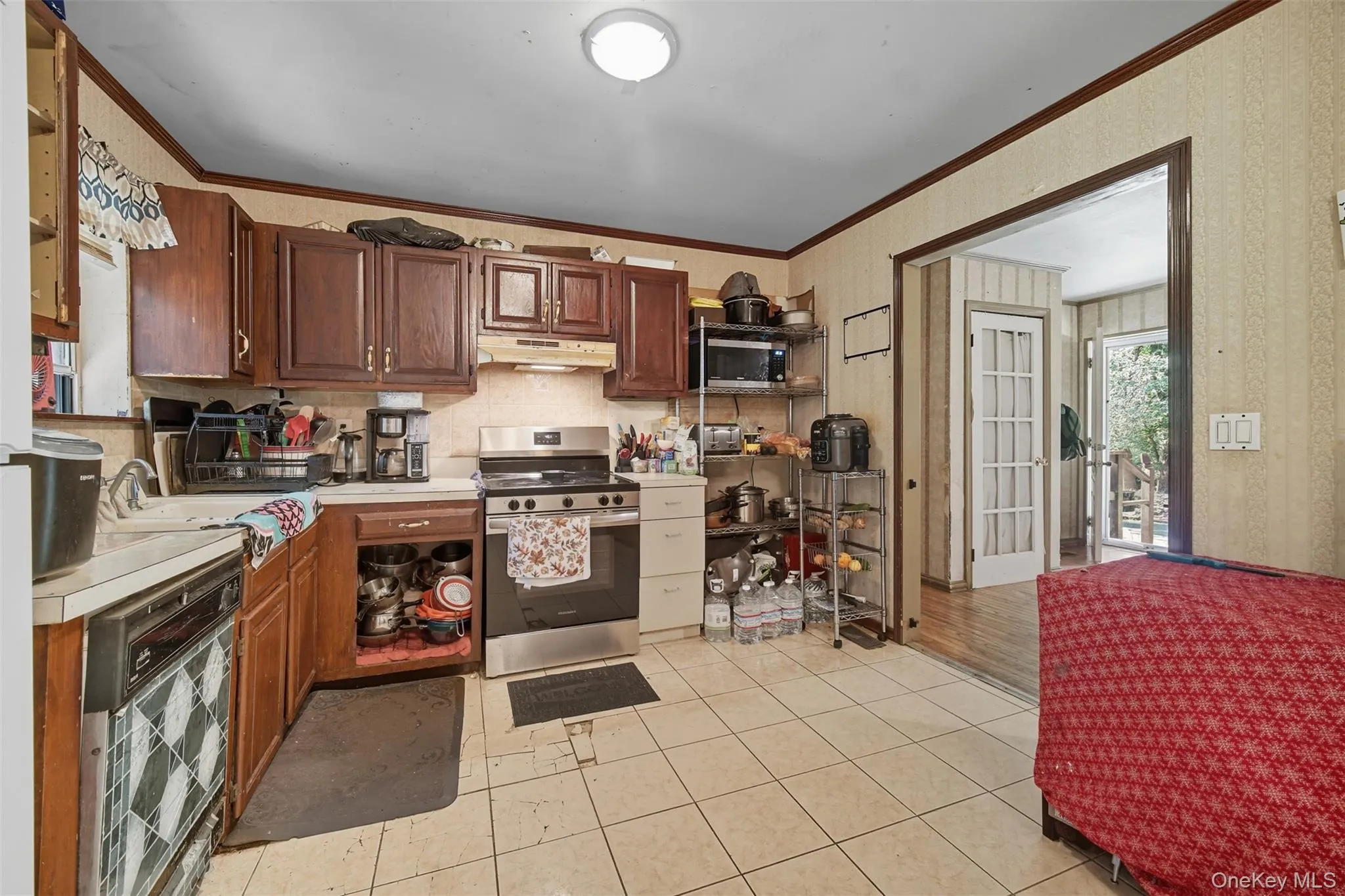 Kitchen featuring open shelves, light countertops, appliances with stainless steel finishes, ornamental molding, and light tile patterned floors Kitchen featuring open shelves, light countertops, appliances with stainless steel finishes, ornamental molding, and light tile patterned floors