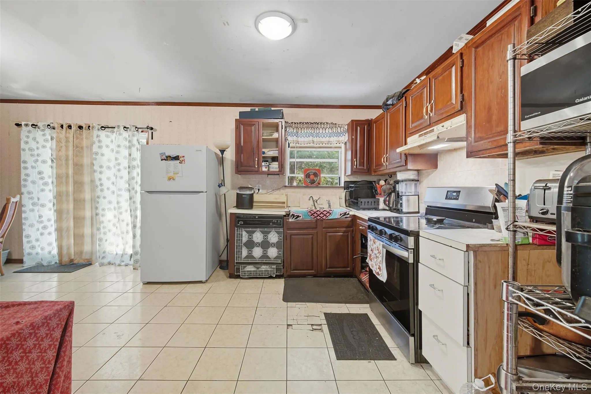 Kitchen featuring light countertops, appliances with stainless steel finishes, crown molding, under cabinet range hood, and decorative backsplash Kitchen featuring light countertops, appliances with stainless steel finishes, crown molding, under cabinet range hood, and decorative backsplash