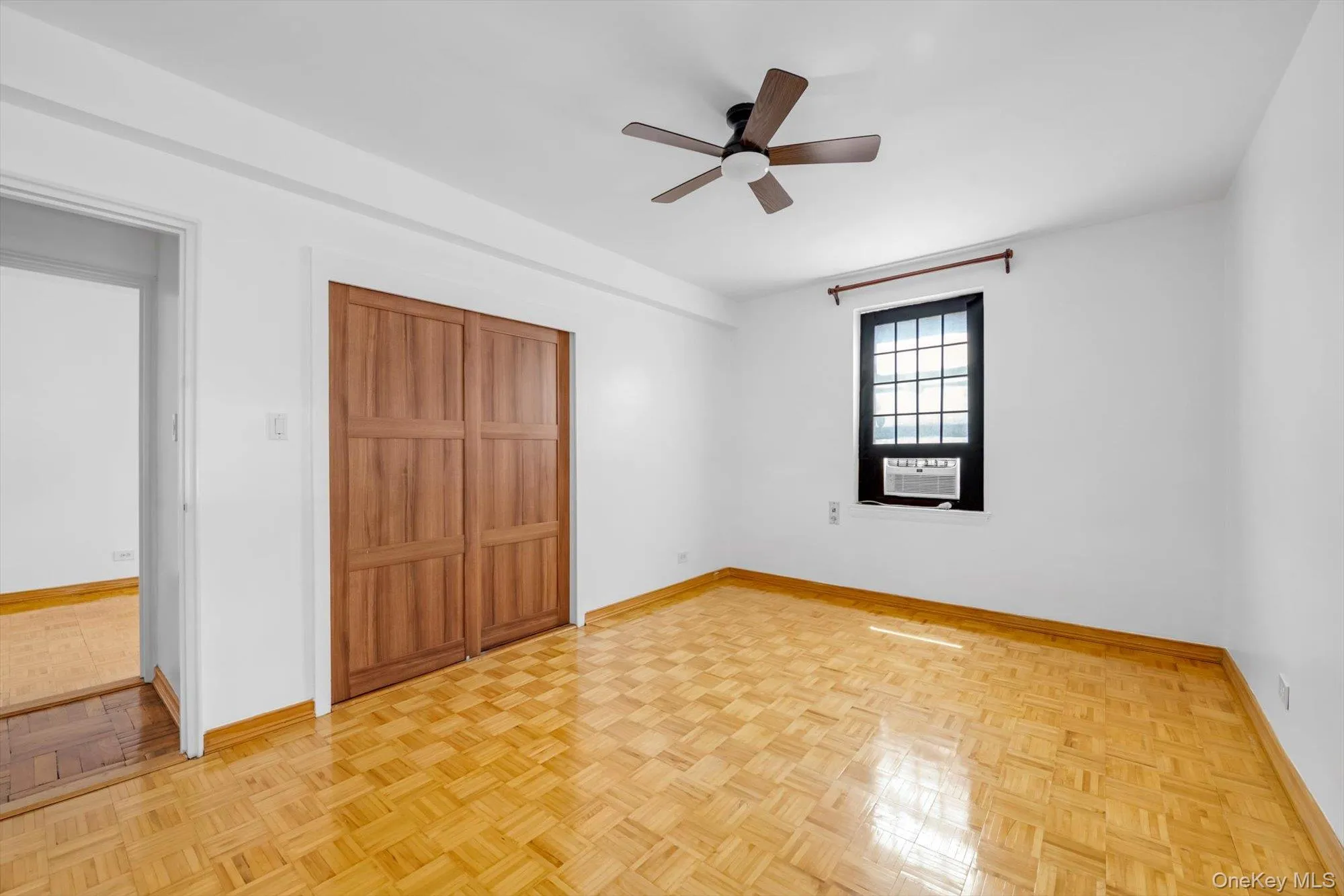 Room featuring parquet flooring, a wood-finish bi-fold closet, a dark-framed window, and a ceiling fan Room featuring parquet flooring, a wood-finish bi-fold closet, a dark-framed window, and a ceiling fan