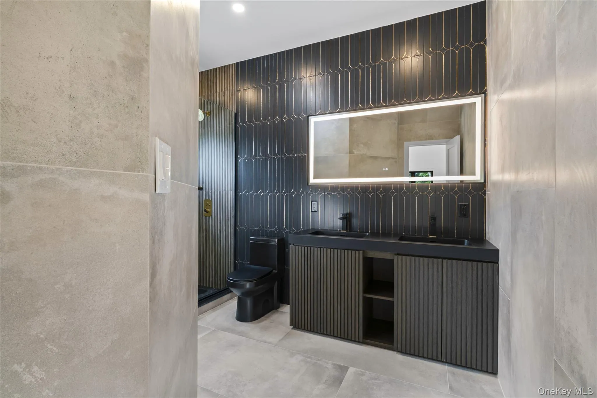 Contemporary bathroom featuring a double vanity with integrated sinks and dark cabinetry, illuminated by a large backlit mirror Contemporary bathroom featuring a double vanity with integrated sinks and dark cabinetry, illuminated by a large backlit mirror