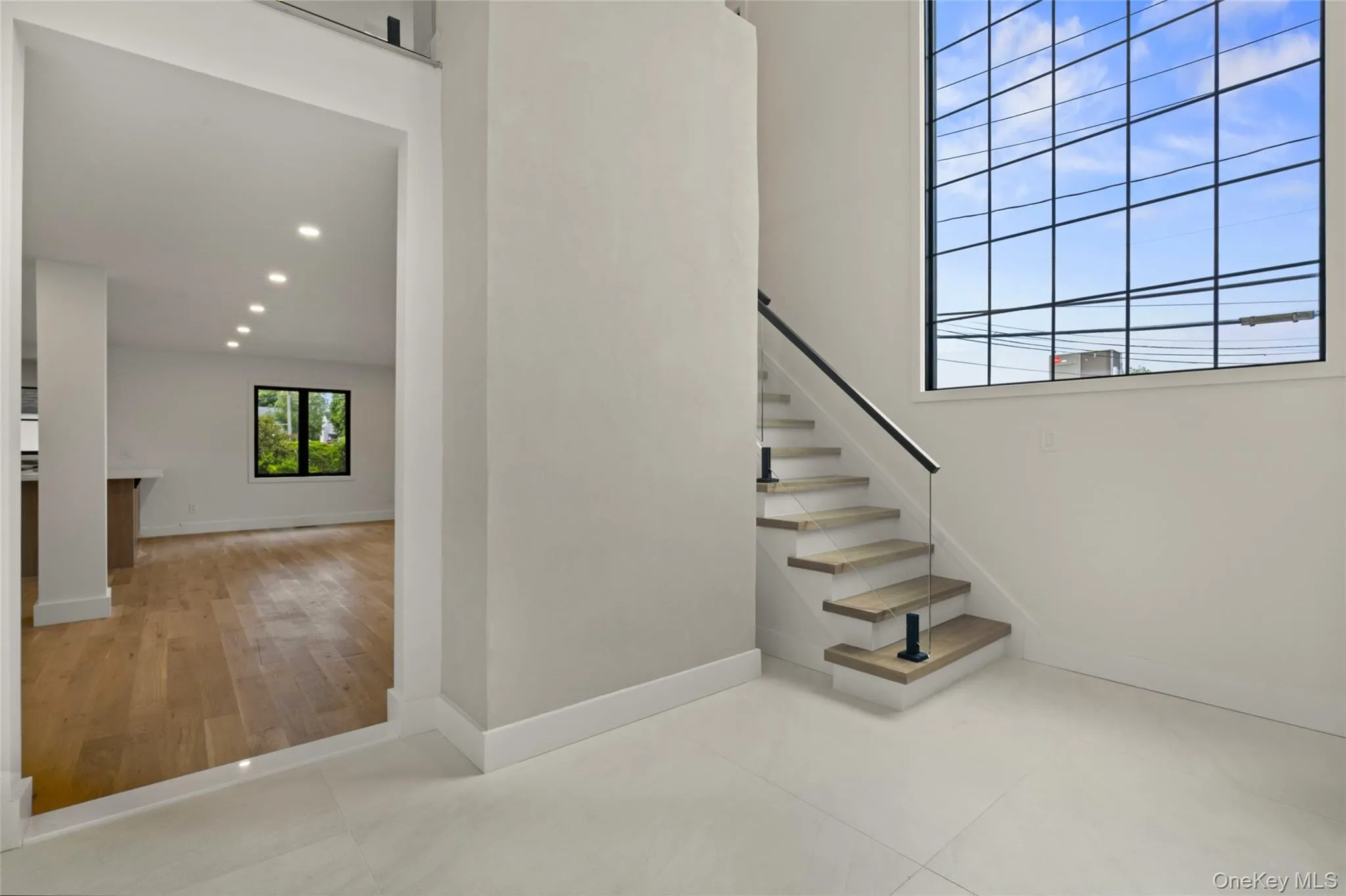 Contemporary staircase featuring wood-finish treads and a glass railing with a black handrail Contemporary staircase featuring wood-finish treads and a glass railing with a black handrail