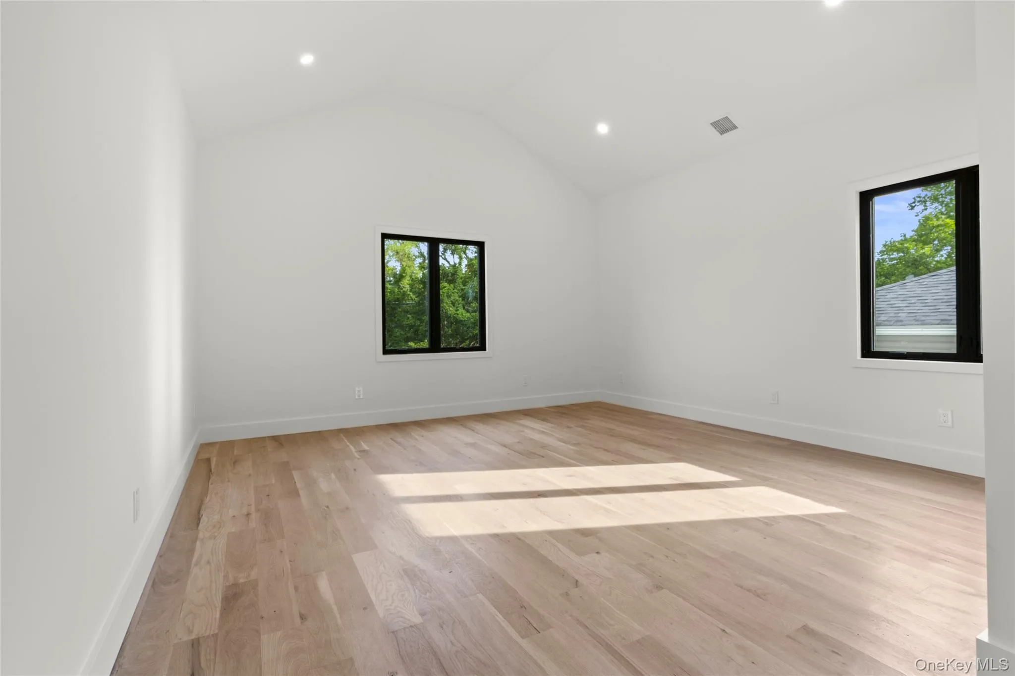 Spacious room featuring vaulted ceilings, recessed lighting, wood-finish flooring, and black-framed windows Spacious room featuring vaulted ceilings, recessed lighting, wood-finish flooring, and black-framed windows