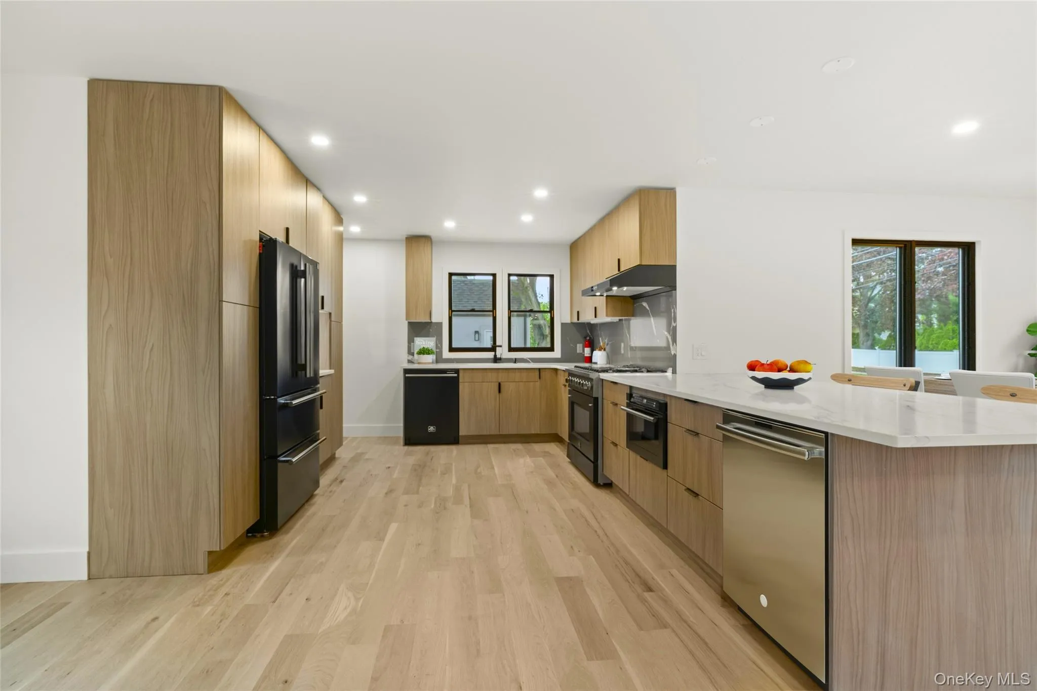 Contemporary kitchen featuring wood-finish cabinetry, a large kitchen island with a stone-finish countertop, stainless steel appliances, and wood-finish flooring Contemporary kitchen featuring wood-finish cabinetry, a large kitchen island with a stone-finish countertop, stainless steel appliances, and wood-finish flooring