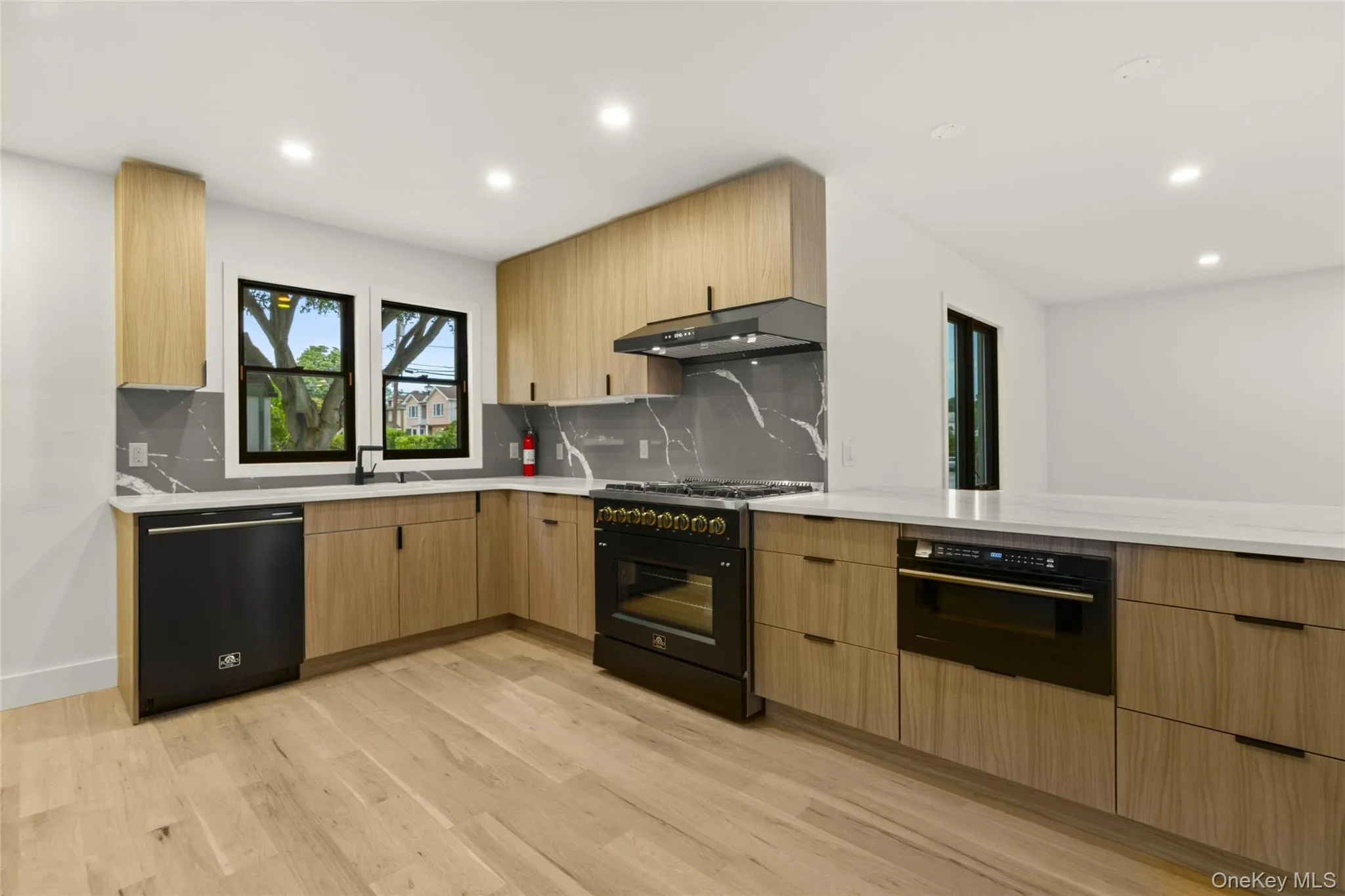 Modern kitchen featuring light wood-finish cabinetry, solid surface countertops, and a full-height stone-look backsplash Modern kitchen featuring light wood-finish cabinetry, solid surface countertops, and a full-height stone-look backsplash