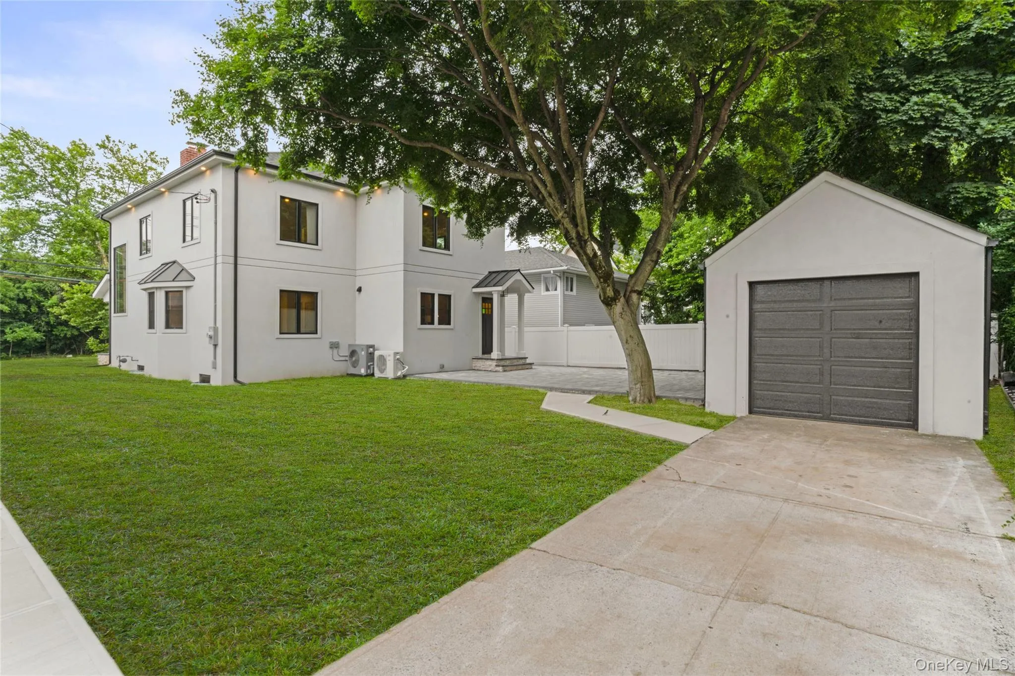 Contemporary white stucco exterior with black-framed windows, a detached single-car garage, mature landscaping, and an expansive lawn Contemporary white stucco exterior with black-framed windows, a detached single-car garage, mature landscaping, and an expansive lawn