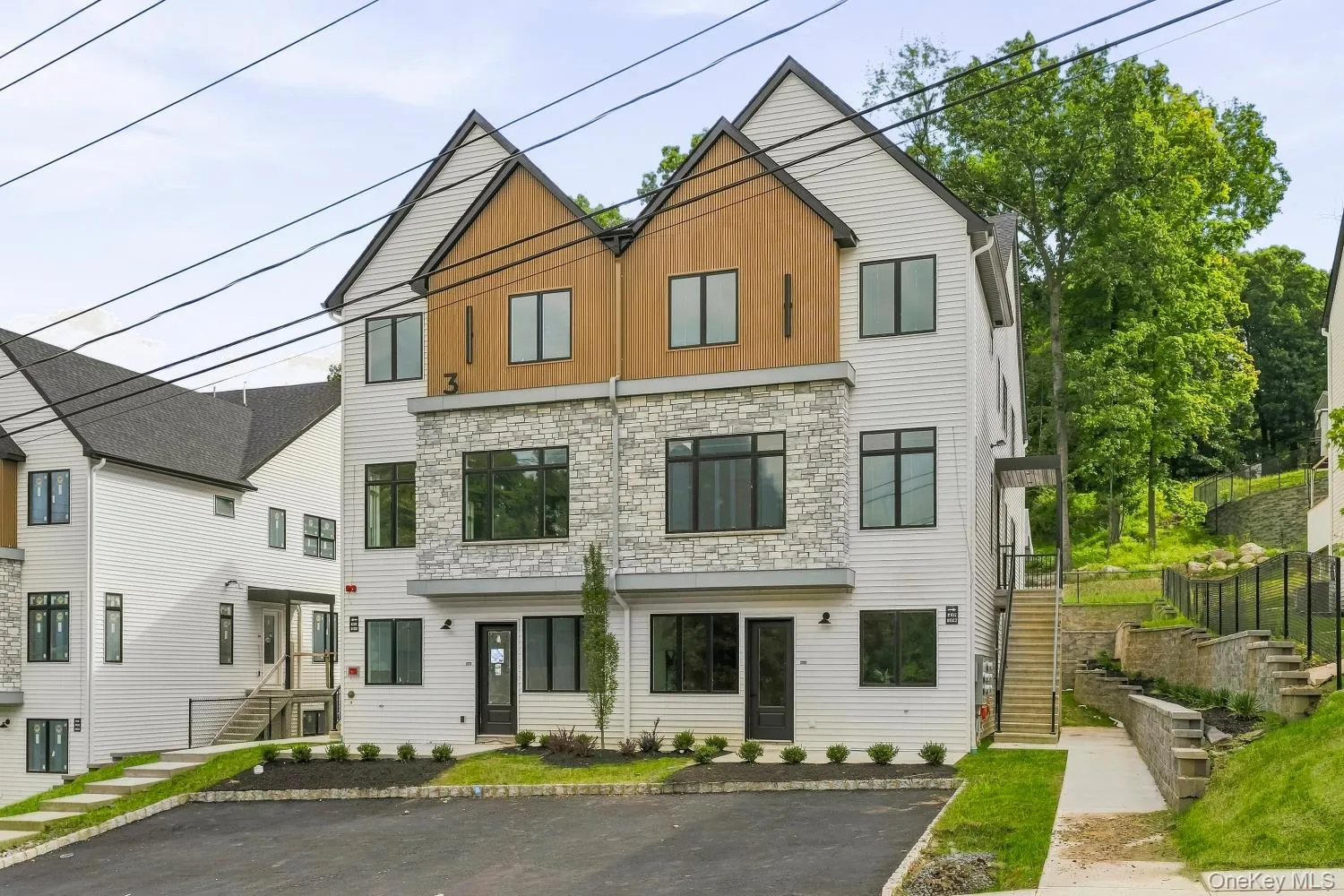 Modern multi-story exterior with white siding, stone accents, and wood-finish paneling Modern multi-story exterior with white siding, stone accents, and wood-finish paneling