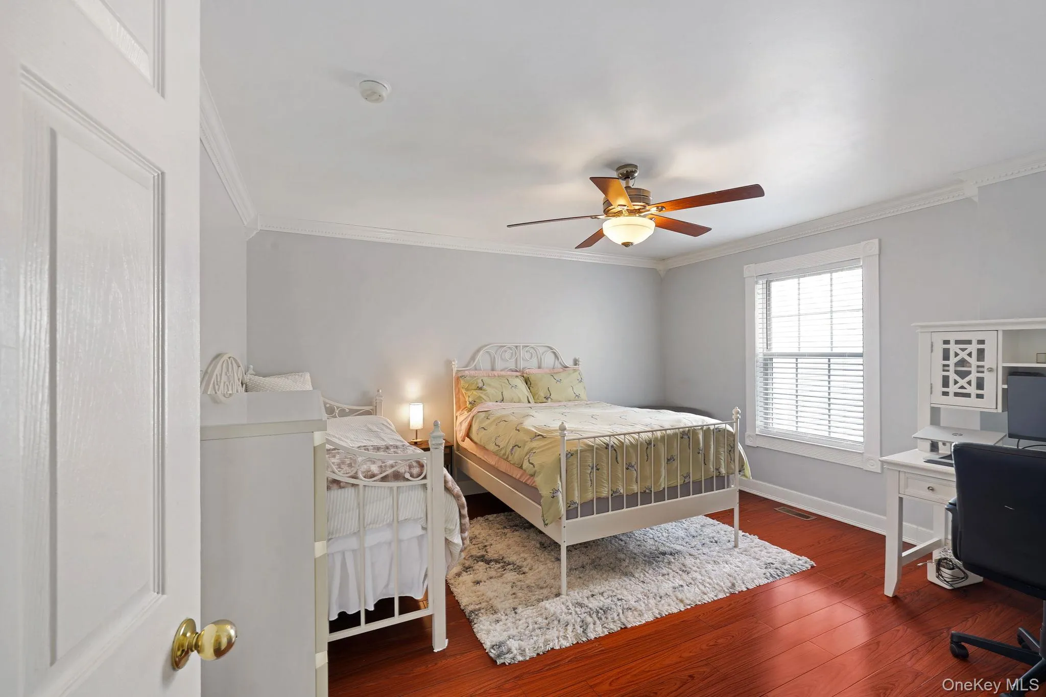 Bedroom featuring wood-finish flooring, a ceiling fan with light fixture, white crown molding, and a white-framed window with blinds Bedroom featuring wood-finish flooring, a ceiling fan with light fixture, white crown molding, and a white-framed window with blinds