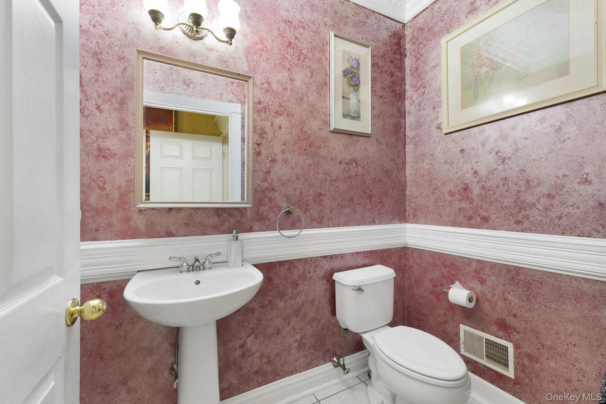 Pedestal sink with a two-handle chrome faucet, illuminated by a three-light vanity fixture Pedestal sink with a two-handle chrome faucet, illuminated by a three-light vanity fixture
