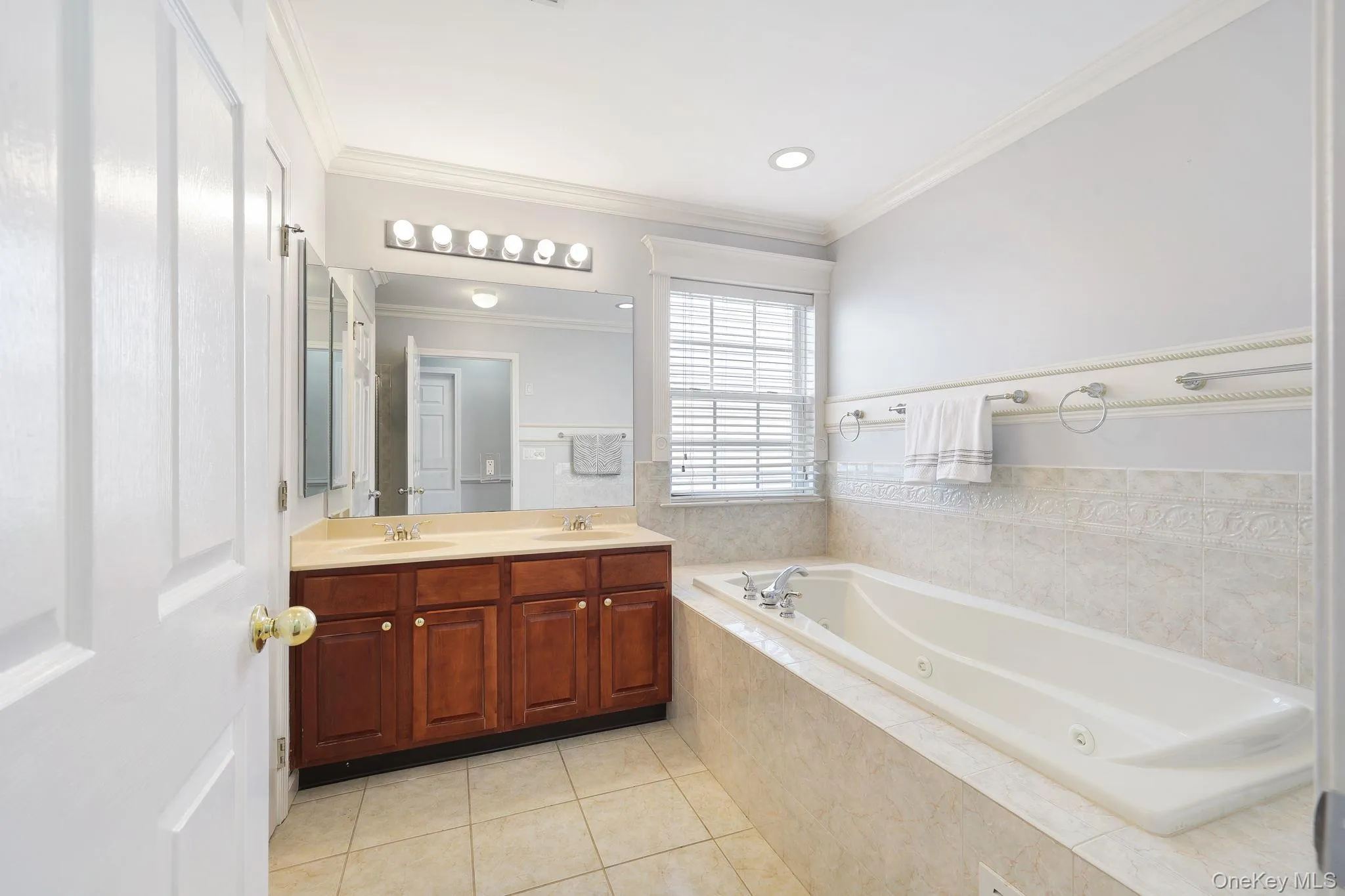 Luxurious bathroom featuring a spacious built-in tub, dual sink vanity with rich wood-finish cabinetry, and tiled flooring Luxurious bathroom featuring a spacious built-in tub, dual sink vanity with rich wood-finish cabinetry, and tiled flooring