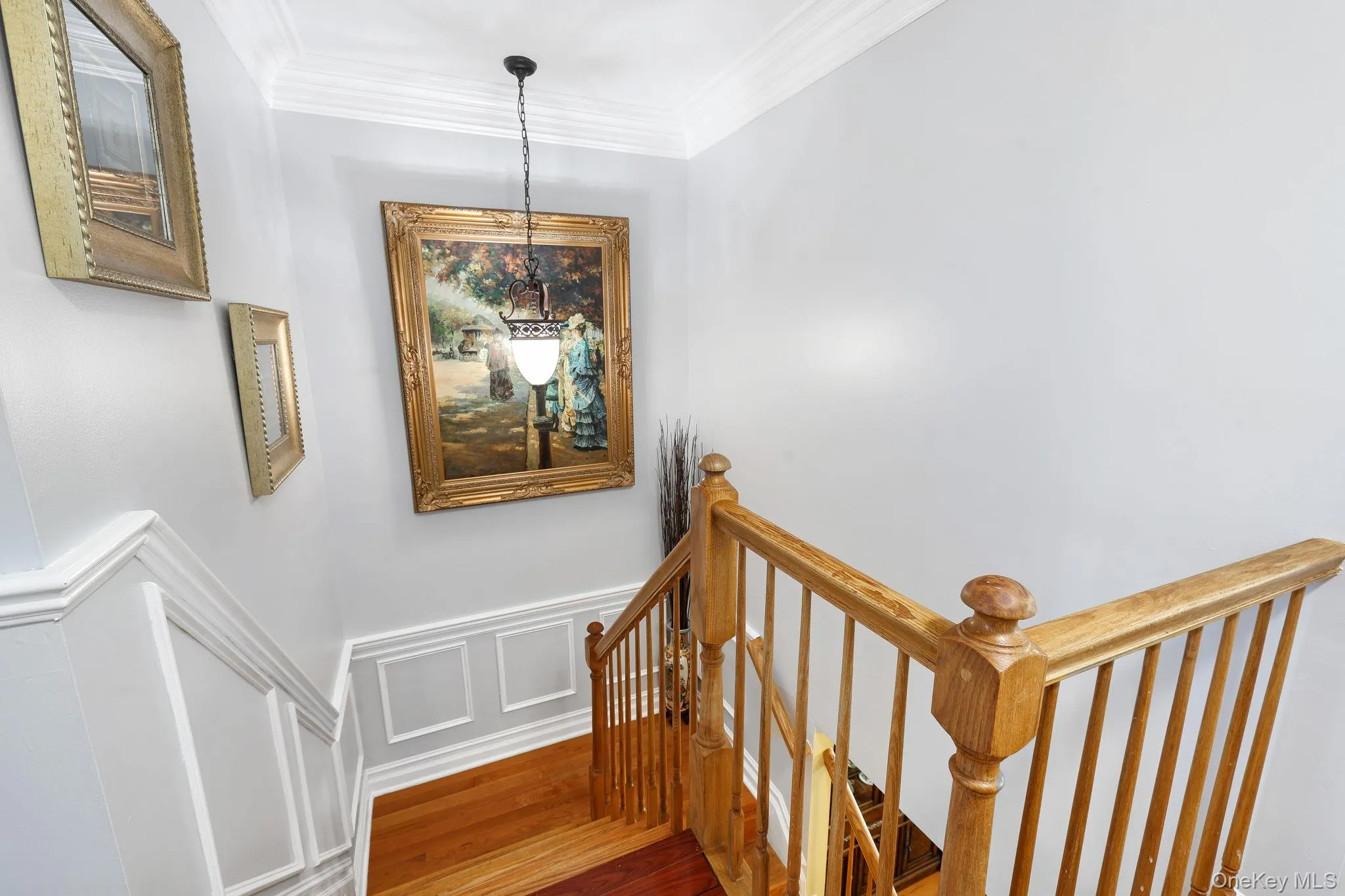 Staircase featuring wood-finish treads and risers, natural wood-finish balustrade, crown molding, wainscoting, and a hanging pendant light fixture Staircase featuring wood-finish treads and risers, natural wood-finish balustrade, crown molding, wainscoting, and a hanging pendant light fixture