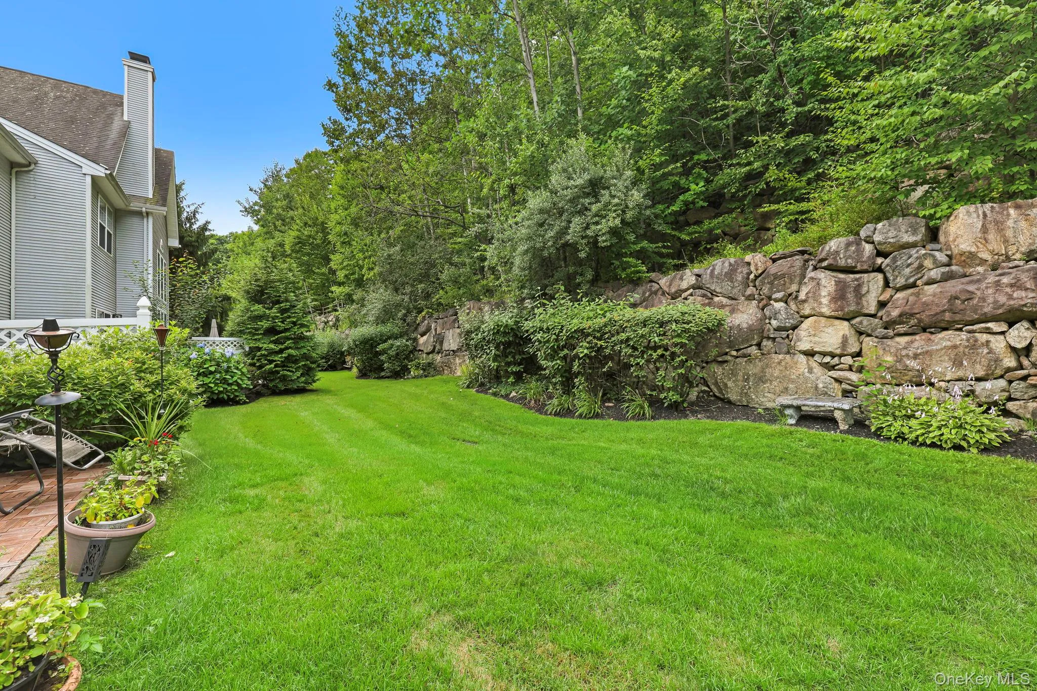 Expansive green lawn bordered by a natural stone retaining wall and mature trees Expansive green lawn bordered by a natural stone retaining wall and mature trees