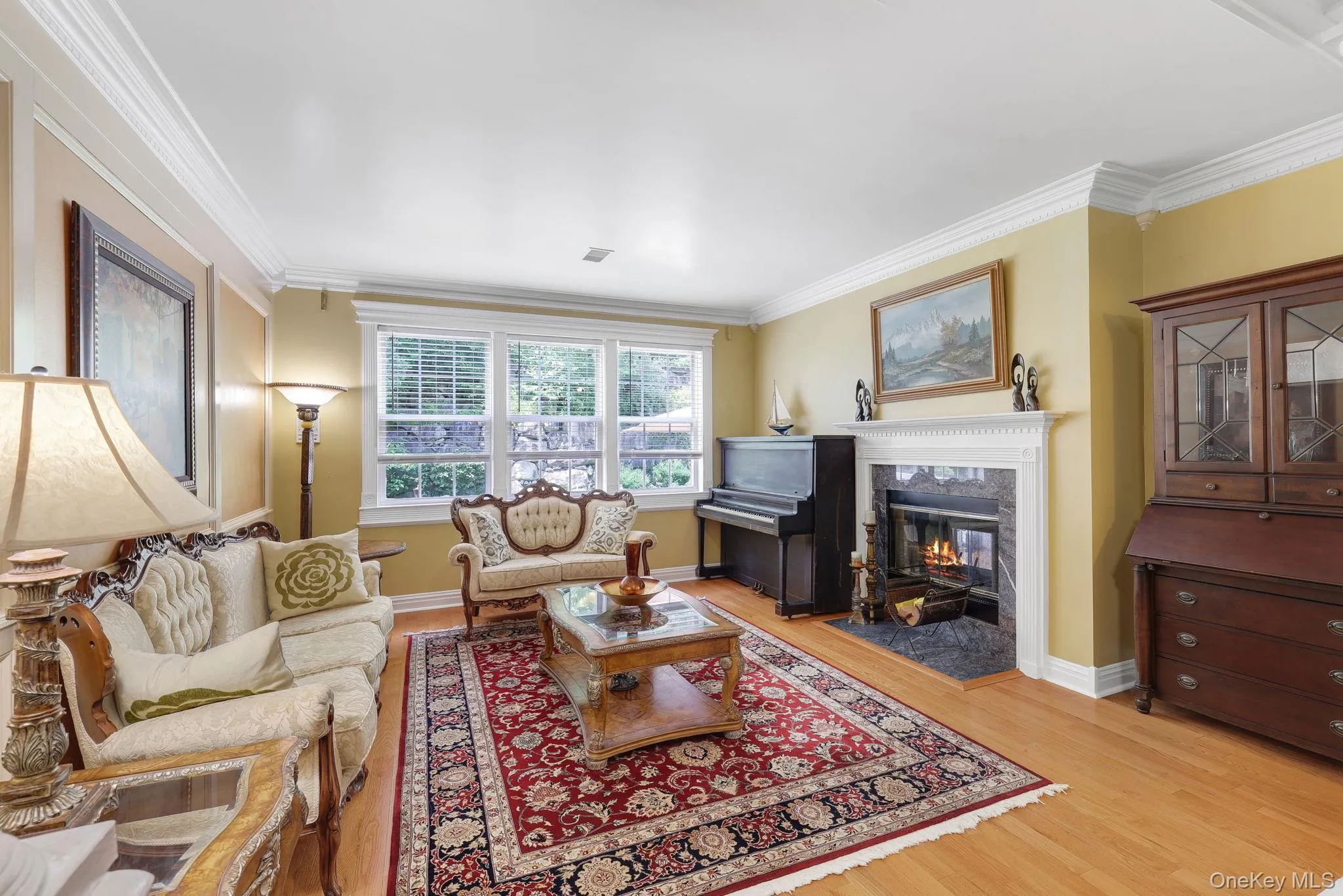 Living area featuring triple windows with traditional fireplace with a white mantel and dark stone surround Living area featuring triple windows with traditional fireplace with a white mantel and dark stone surround