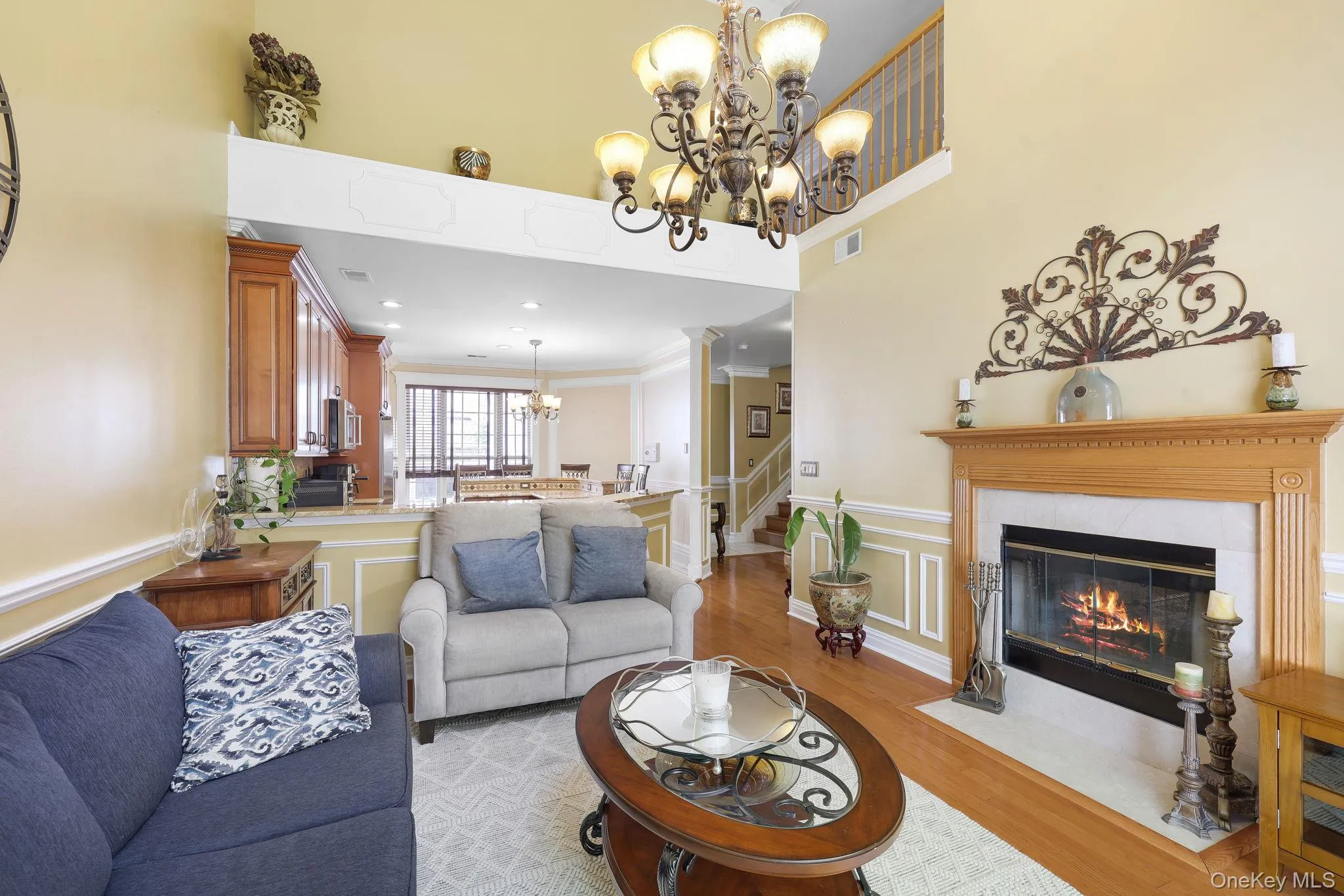 Living area featuring a fireplace with a wood-finish mantel and stone surround, wood-finish flooring, and a two-story ceiling Living area featuring a fireplace with a wood-finish mantel and stone surround, wood-finish flooring, and a two-story ceiling
