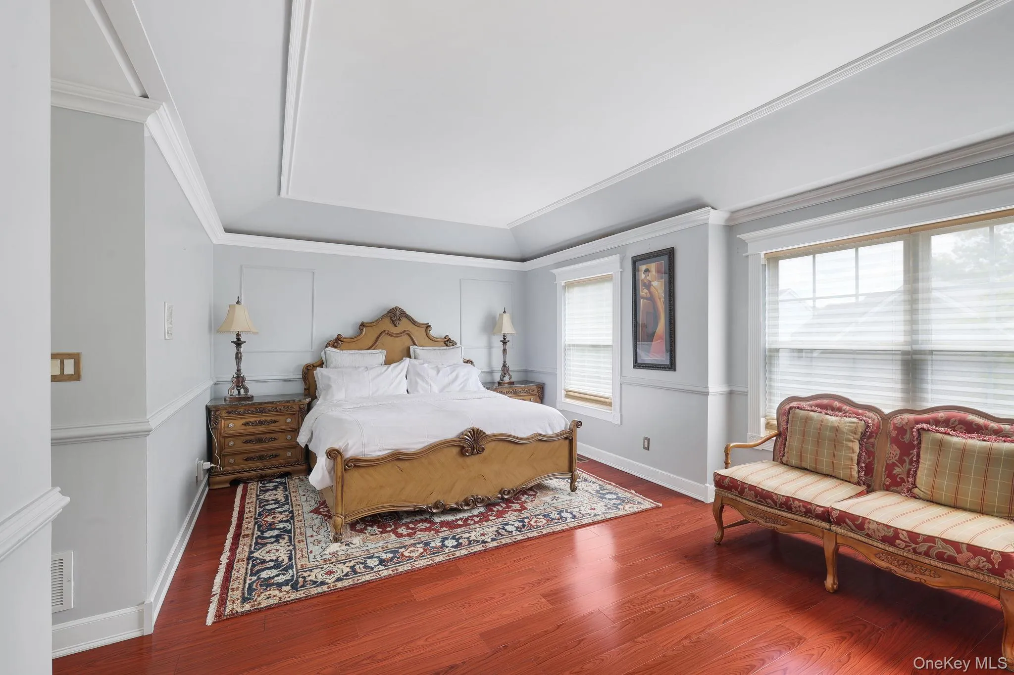 Bedroom featuring rich wood-finish flooring, a tray ceiling, and extensive crown molding Bedroom featuring rich wood-finish flooring, a tray ceiling, and extensive crown molding