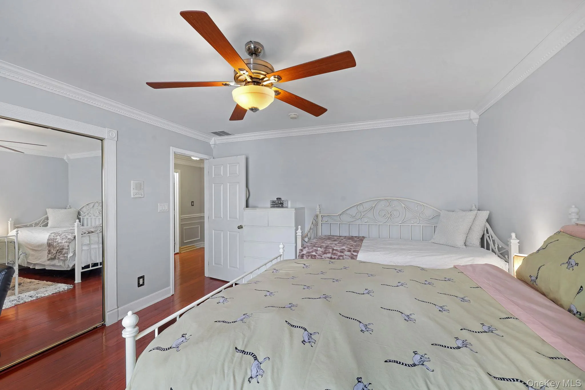 Bedroom featuring rich wood-finish flooring, a ceiling fan with integrated lighting, mirrored closet doors, crown molding, and a paneled interior door Bedroom featuring rich wood-finish flooring, a ceiling fan with integrated lighting, mirrored closet doors, crown molding, and a paneled interior door