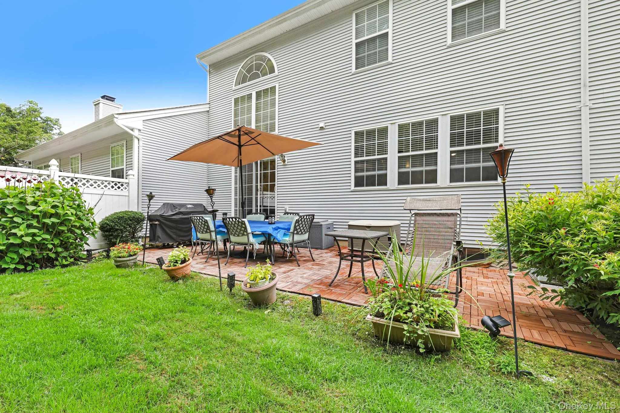 Expansive brick paver patio featuring direct access to the interior via double French doors, complemented by a manicured lawn and mature plantings Expansive brick paver patio featuring direct access to the interior via double French doors, complemented by a manicured lawn and mature plantings