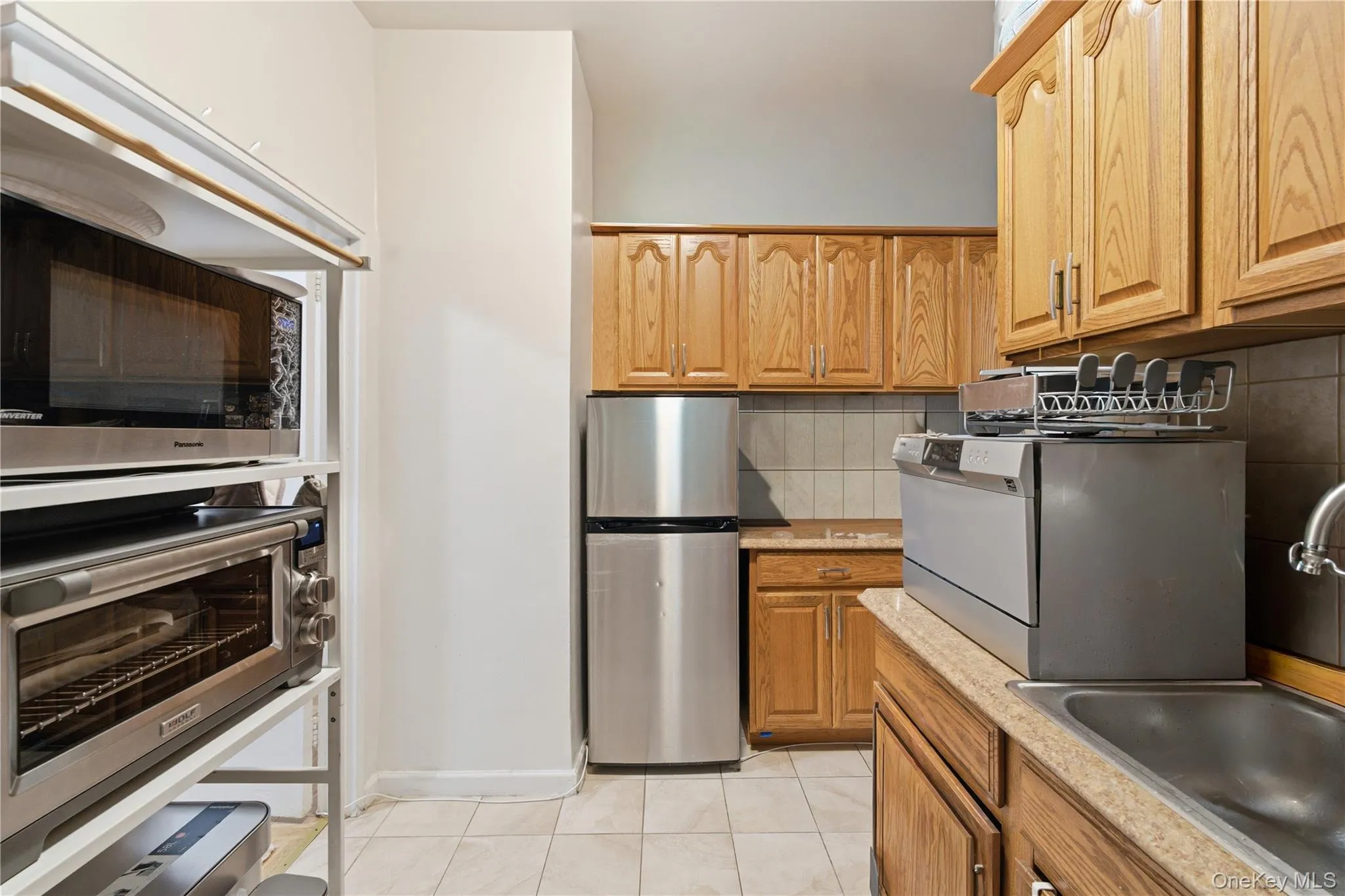 Kitchen featuring wood cabinetry, stainless steel refrigerator, and tiled flooring Kitchen featuring wood cabinetry, stainless steel refrigerator, and tiled flooring