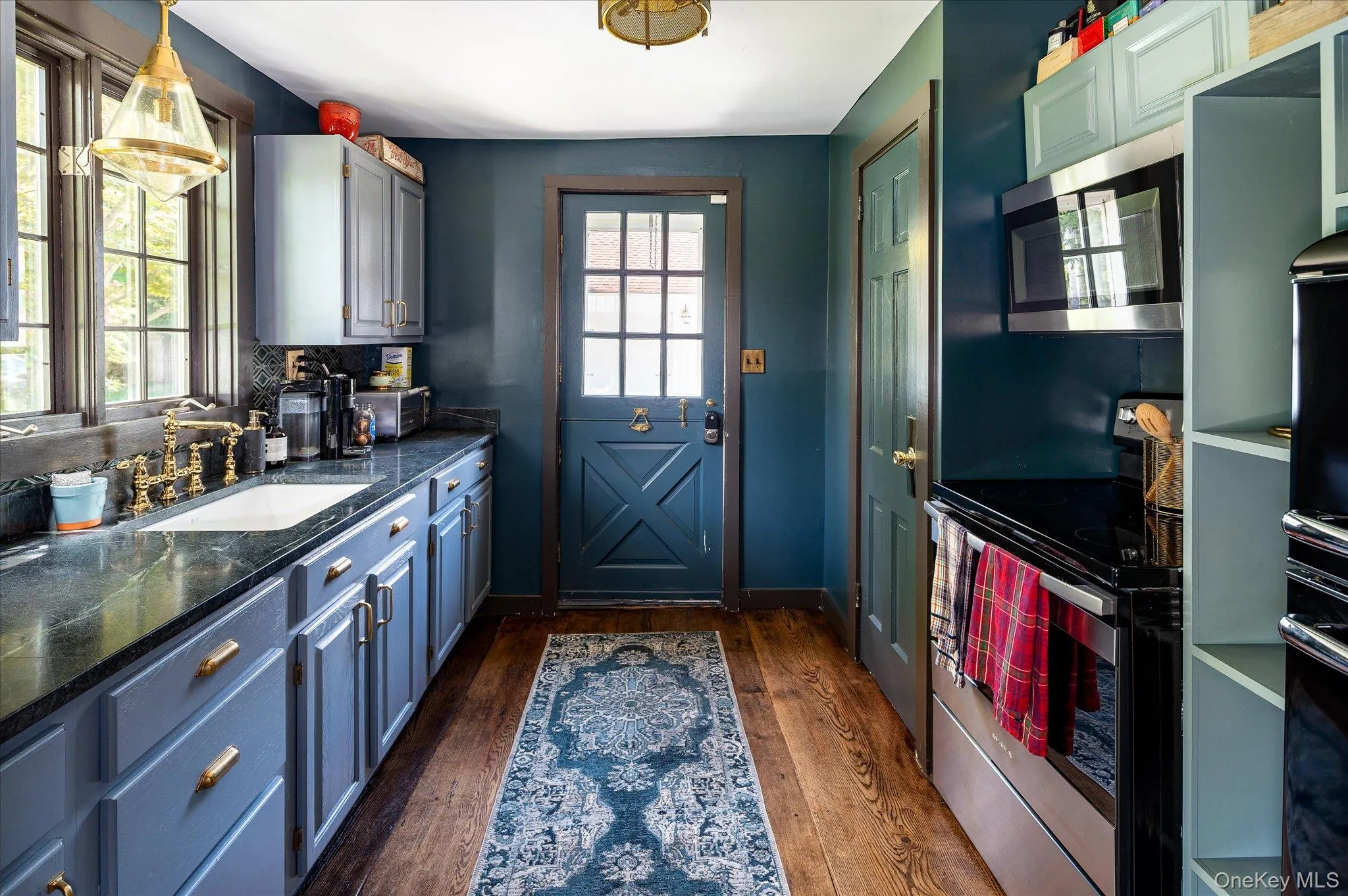 Kitchen featuring appliances with stainless steel finishes, dark wood-style flooring, blue cabinets, hanging light fixtures, and dark stone countertops Kitchen featuring appliances with stainless steel finishes, dark wood-style flooring, blue cabinets, hanging light fixtures, and dark stone countertops