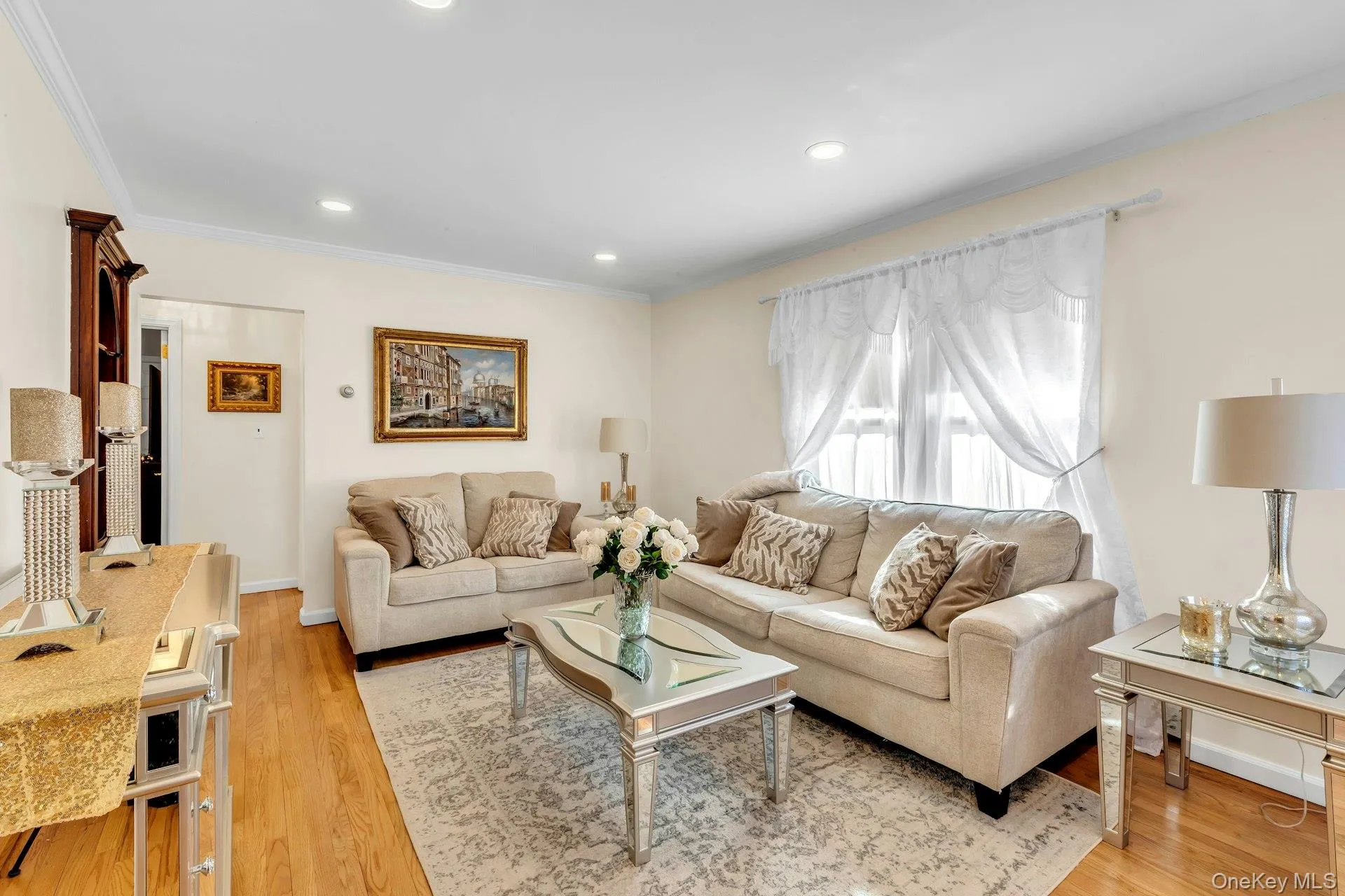 Living area featuring recessed lighting, crown molding, wood-finish flooring, and a large window with sheer drapery Living area featuring recessed lighting, crown molding, wood-finish flooring, and a large window with sheer drapery