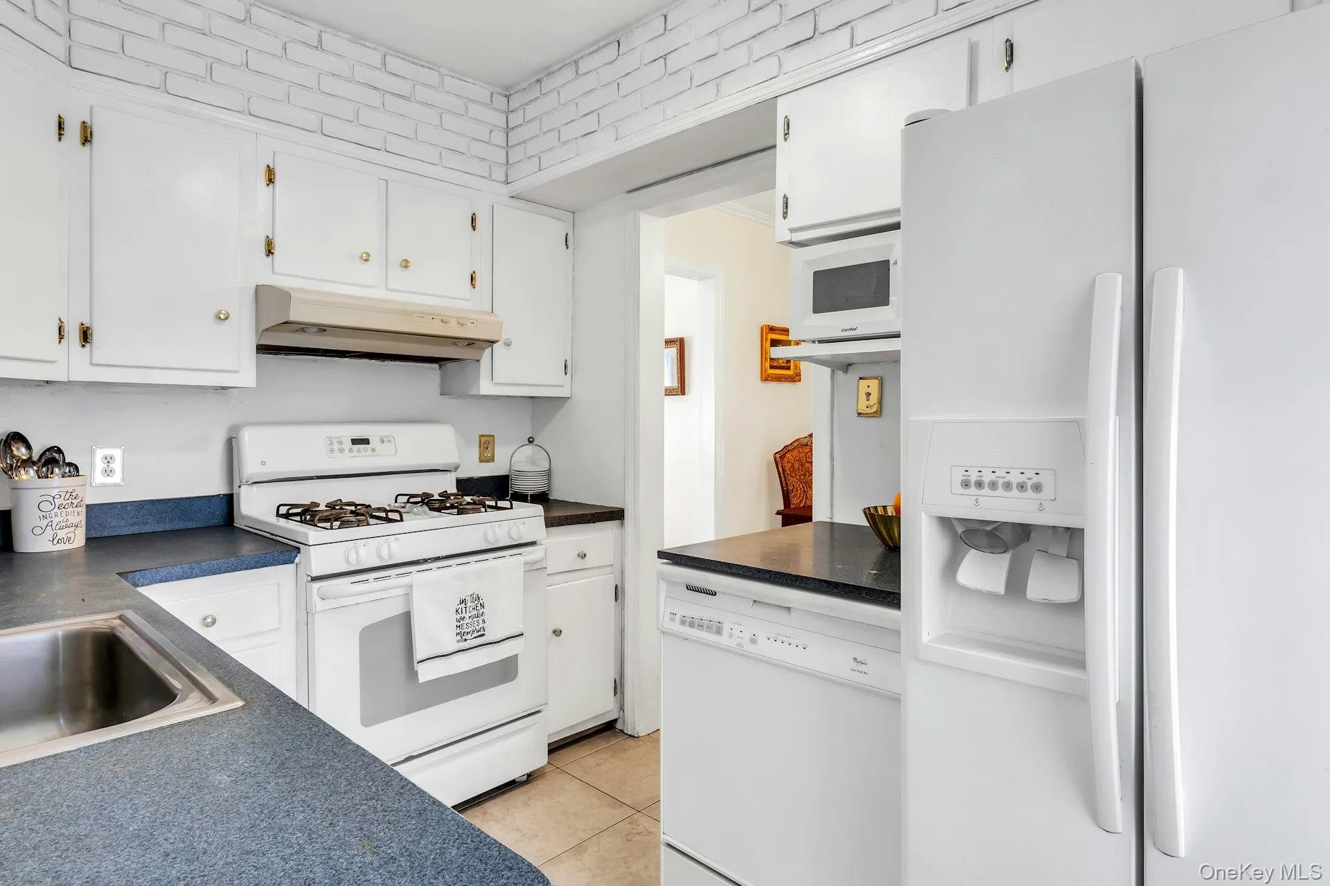 Kitchen featuring white cabinetry with gold-toned hardware, a gas range with an overhead exhaust, a stainless steel sink, and a side-by-side refrigerator with an ice and water dispenser Kitchen featuring white cabinetry with gold-toned hardware, a gas range with an overhead exhaust, a stainless steel sink, and a side-by-side refrigerator with an ice and water dispenser