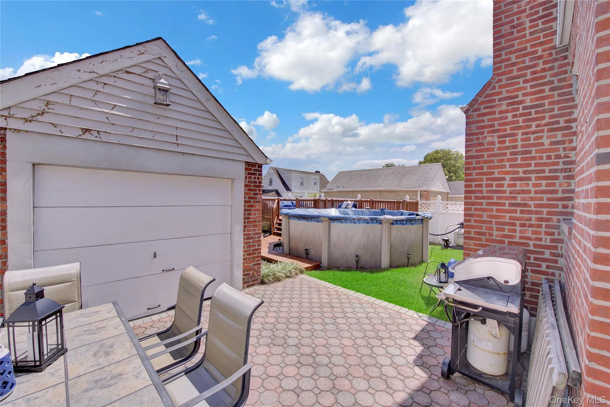 Rear exterior featuring a brick facade, detached garage with white paneling, paver patio, and an above-ground pool Rear exterior featuring a brick facade, detached garage with white paneling, paver patio, and an above-ground pool