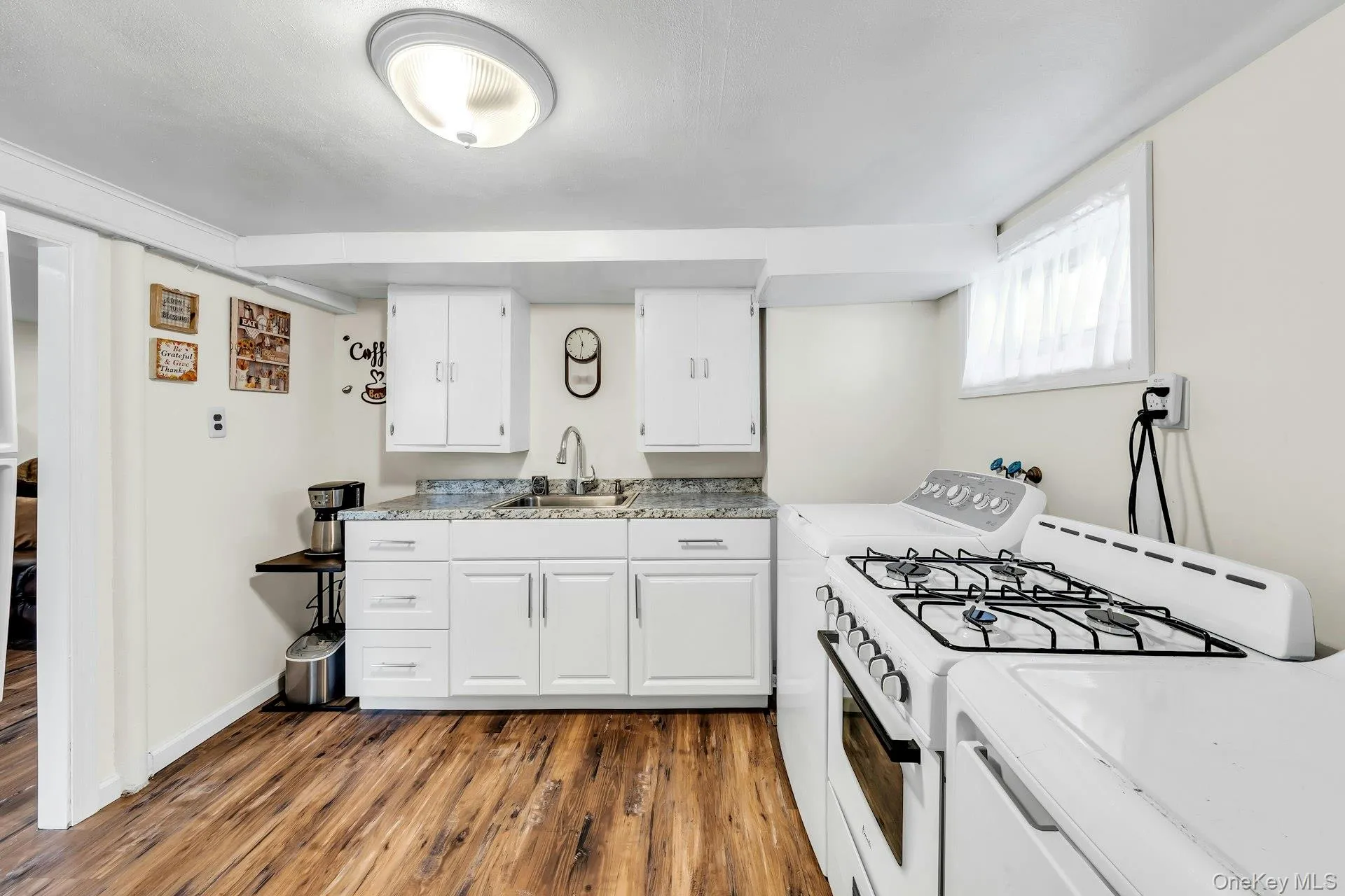 Compact kitchen area featuring white cabinetry, a stainless steel sink with a high-arc faucet, and granite-style countertops Compact kitchen area featuring white cabinetry, a stainless steel sink with a high-arc faucet, and granite-style countertops