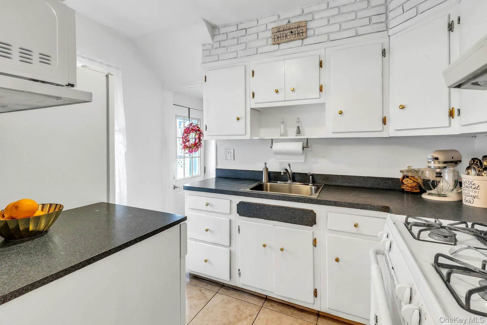 Kitchen featuring white cabinetry with brass hardware, dark countertops, a stainless steel sink, and a white gas range Kitchen featuring white cabinetry with brass hardware, dark countertops, a stainless steel sink, and a white gas range
