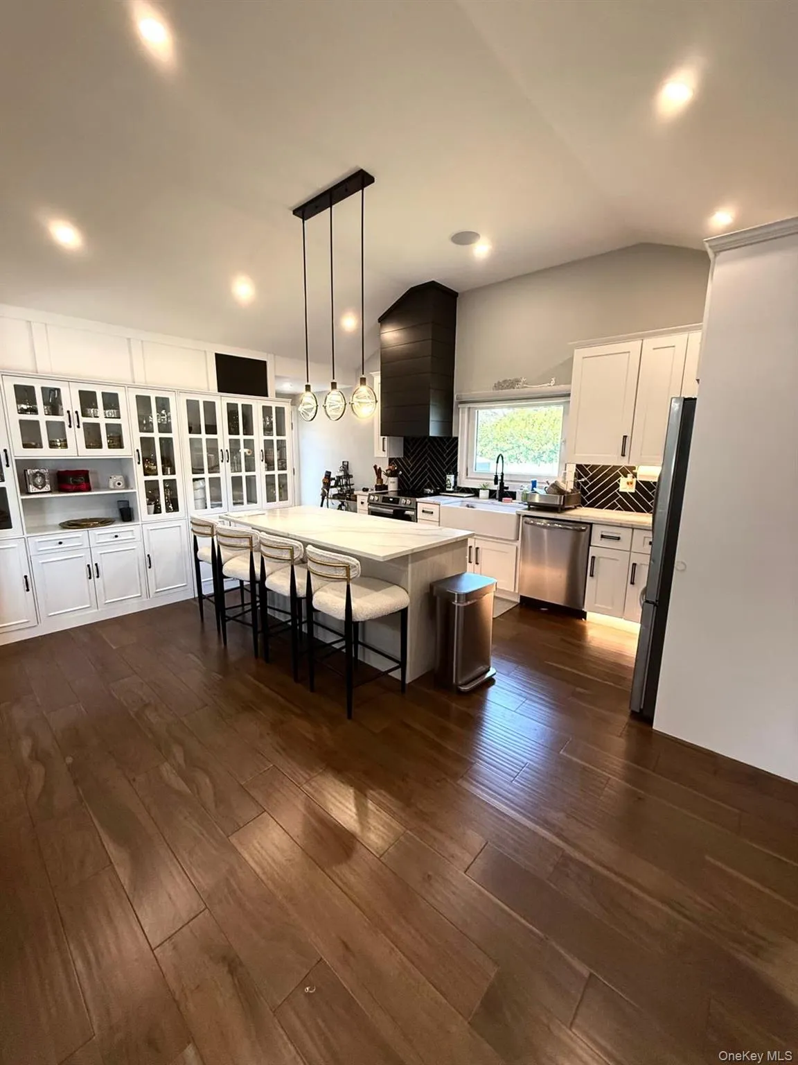 Expansive kitchen featuring a large central island with seating, a dark wood-finish range hood, and white cabinetry Expansive kitchen featuring a large central island with seating, a dark wood-finish range hood, and white cabinetry