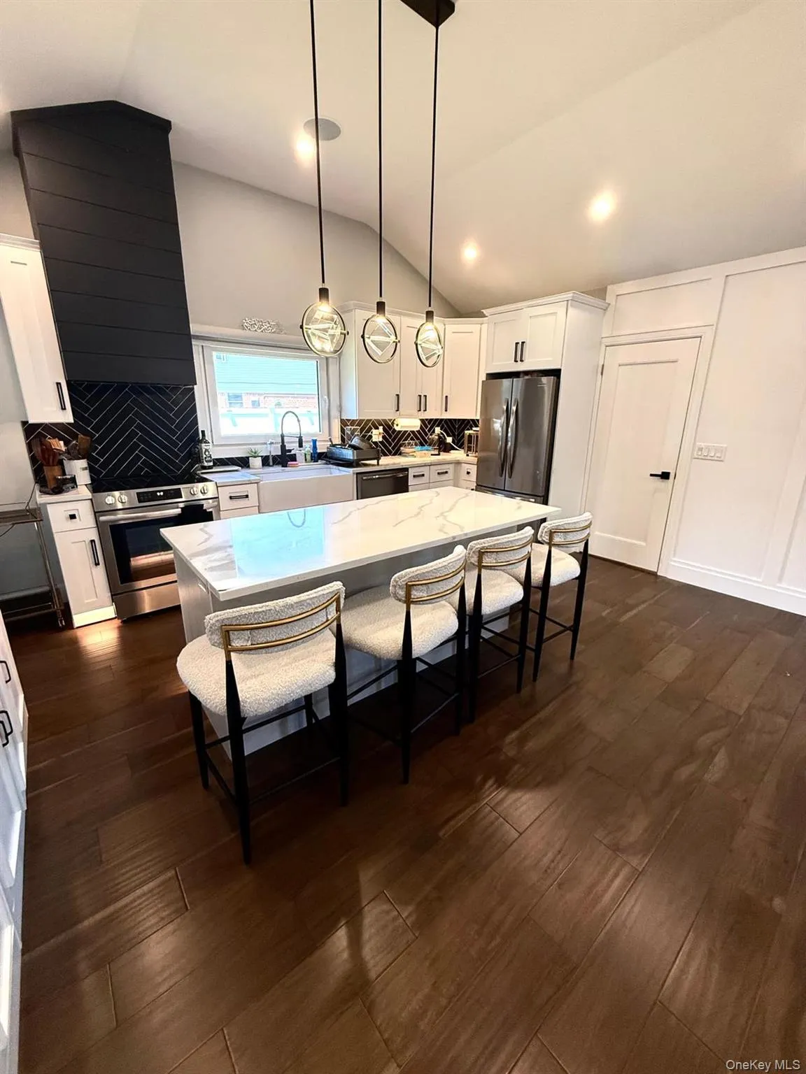 Modern kitchen featuring wood-finish flooring, white cabinetry with dark hardware, and a white quartz-finish island with seating Modern kitchen featuring wood-finish flooring, white cabinetry with dark hardware, and a white quartz-finish island with seating