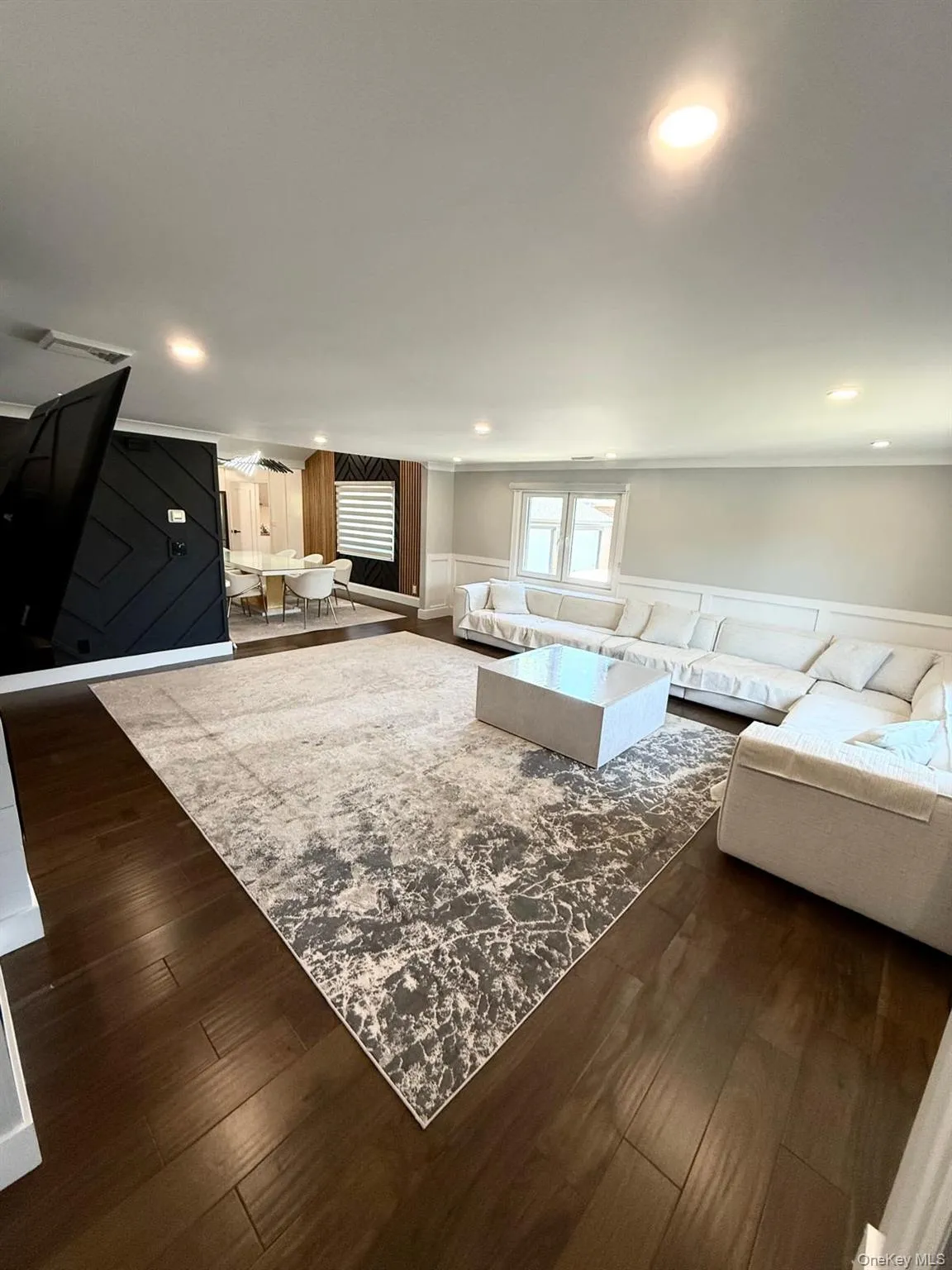 Spacious living area featuring dark wood-finish flooring, recessed lighting, built in electric fireplace and a large window with white trim Spacious living area featuring dark wood-finish flooring, recessed lighting, built in electric fireplace and a large window with white trim