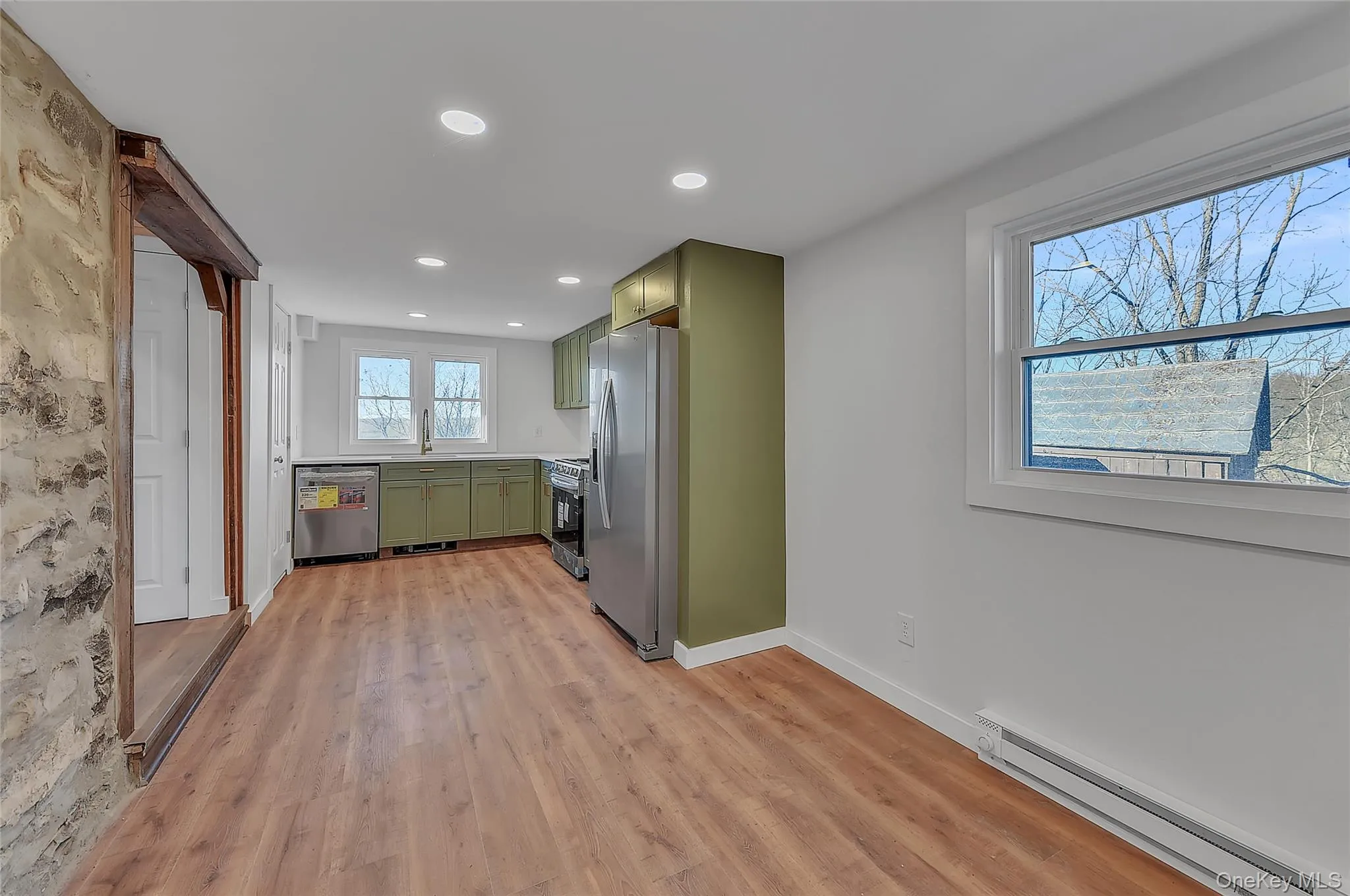 Kitchen with green cabinets, baseboard heating, stainless steel appliances, light countertops, and light wood finished floors Kitchen with green cabinets, baseboard heating, stainless steel appliances, light countertops, and light wood finished floors