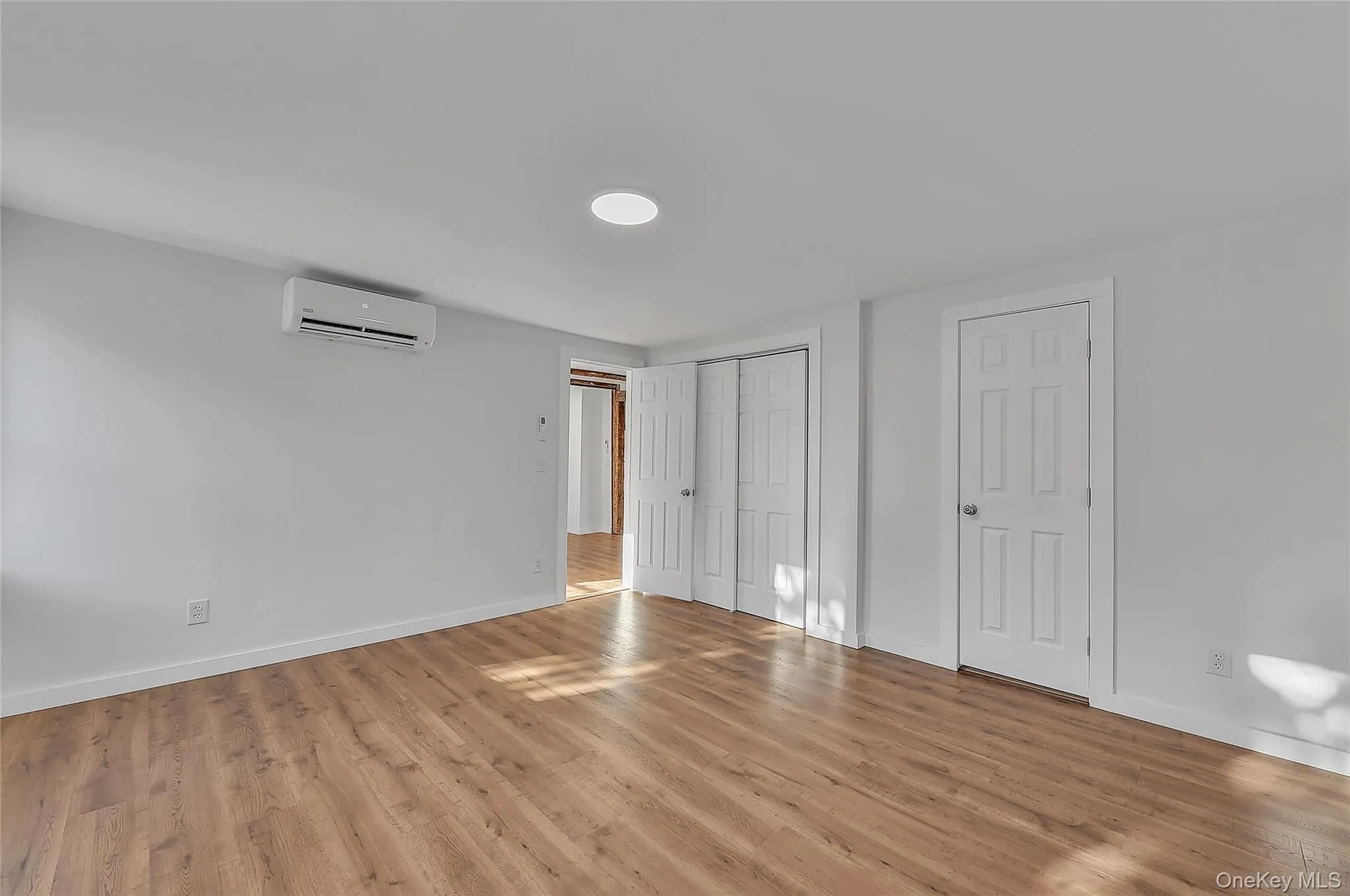 Unfurnished bedroom with wood finished floors and a wall mounted AC Unfurnished bedroom with wood finished floors and a wall mounted AC
