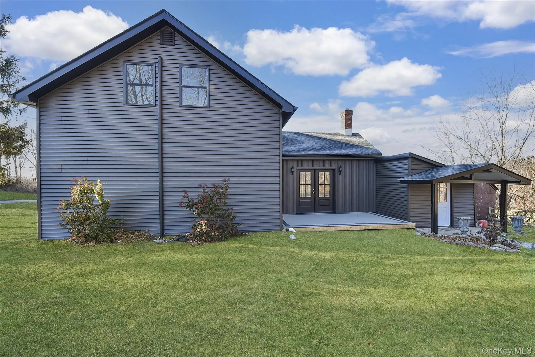 Back of property featuring a lawn, a shingled roof, a deck, and a chimney Back of property featuring a lawn, a shingled roof, a deck, and a chimney