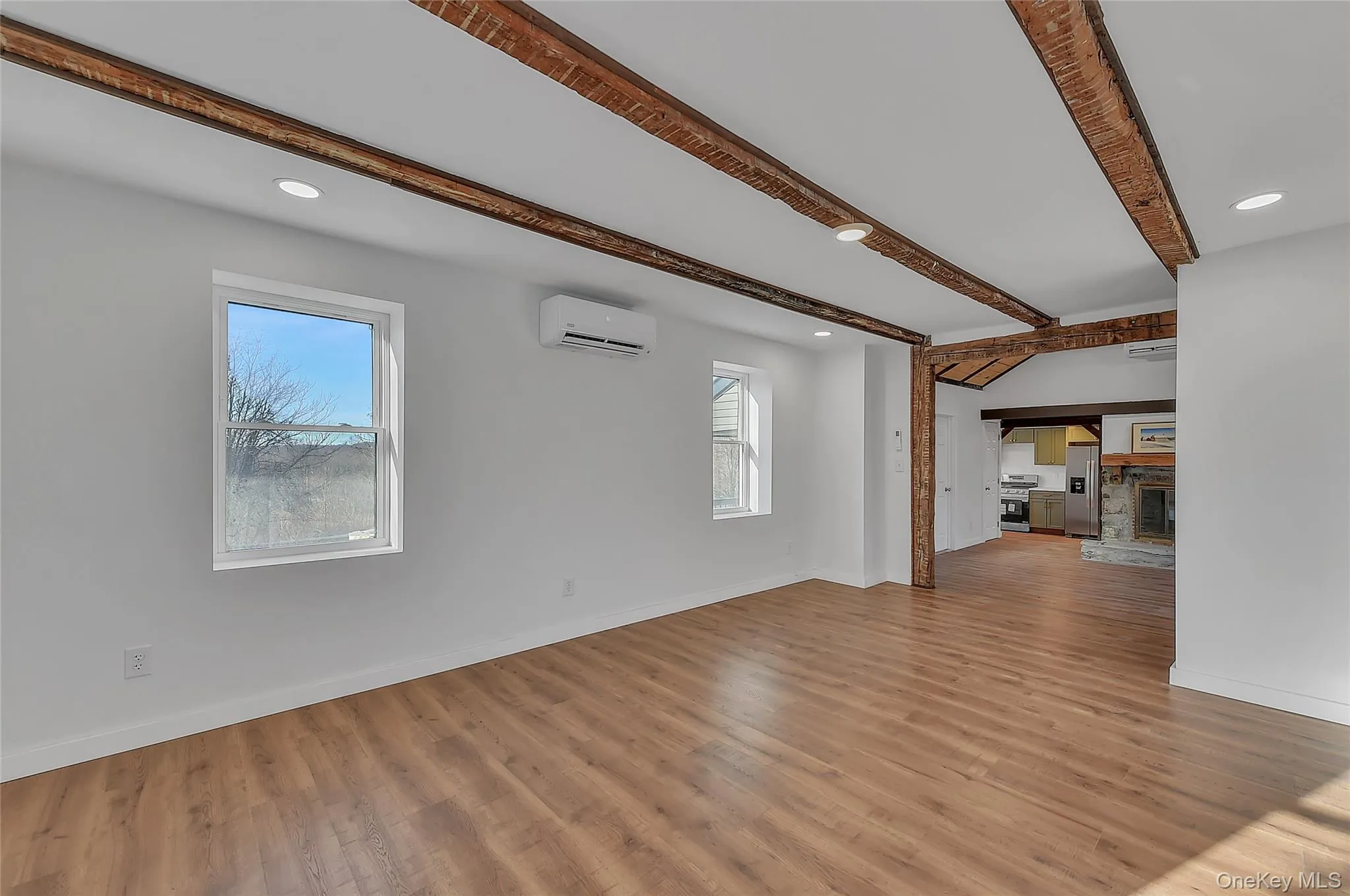 Unfurnished living room featuring recessed lighting, a stone fireplace, beam ceiling, light wood-style flooring, and a wall unit AC Unfurnished living room featuring recessed lighting, a stone fireplace, beam ceiling, light wood-style flooring, and a wall unit AC