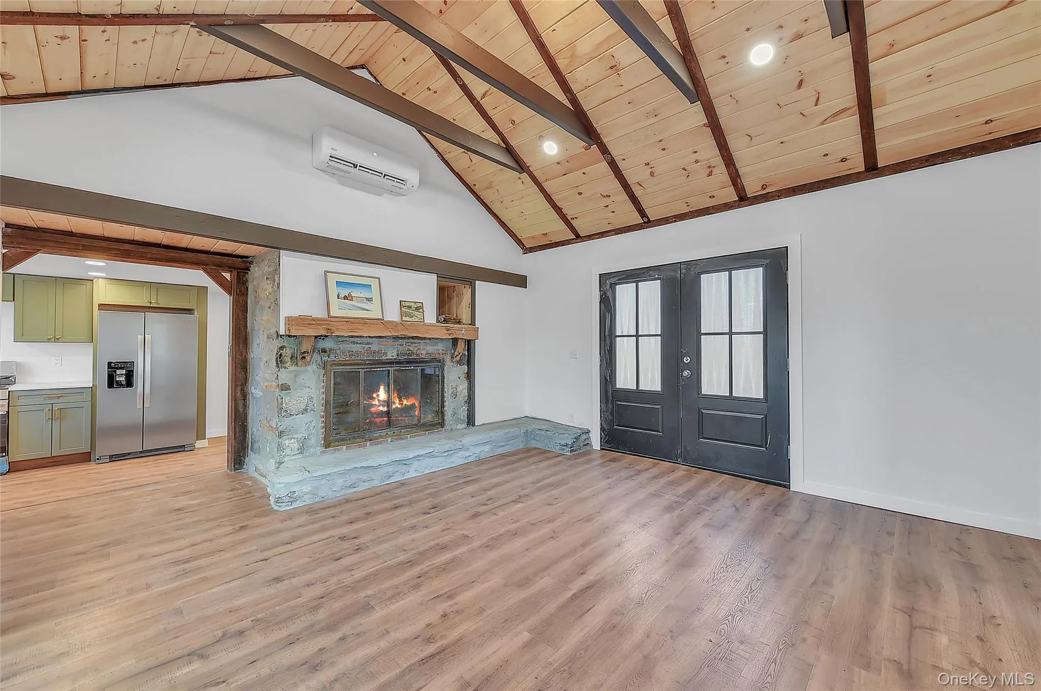 Unfurnished living room with french doors, high vaulted ceiling, a wood ceiling with exposed beams, a wall mounted AC, and light wood-style floors Unfurnished living room with french doors, high vaulted ceiling, a wood ceiling with exposed beams, a wall mounted AC, and light wood-style floors