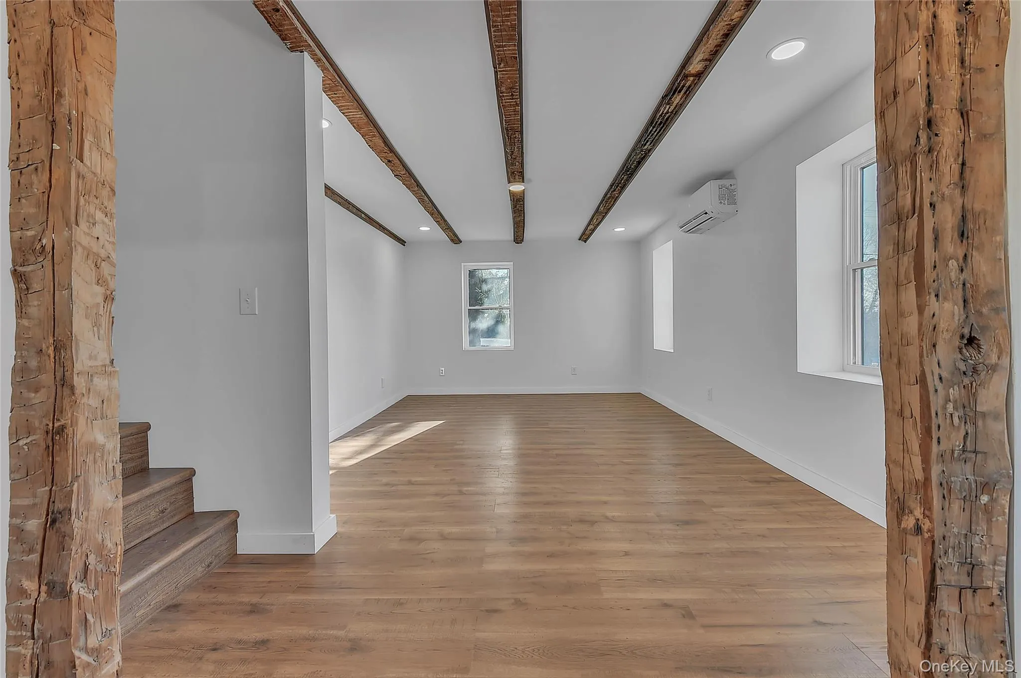 Unfurnished living room with recessed lighting, beam ceiling, light wood-style floors, and an AC wall unit Unfurnished living room with recessed lighting, beam ceiling, light wood-style floors, and an AC wall unit
