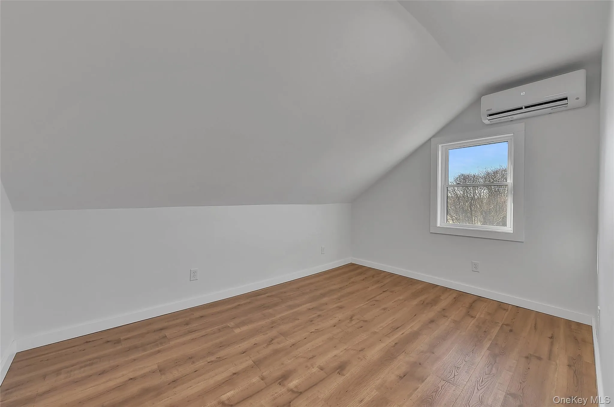 Additional living space with vaulted ceiling, light wood-style floors, and a wall mounted air conditioner Additional living space with vaulted ceiling, light wood-style floors, and a wall mounted air conditioner