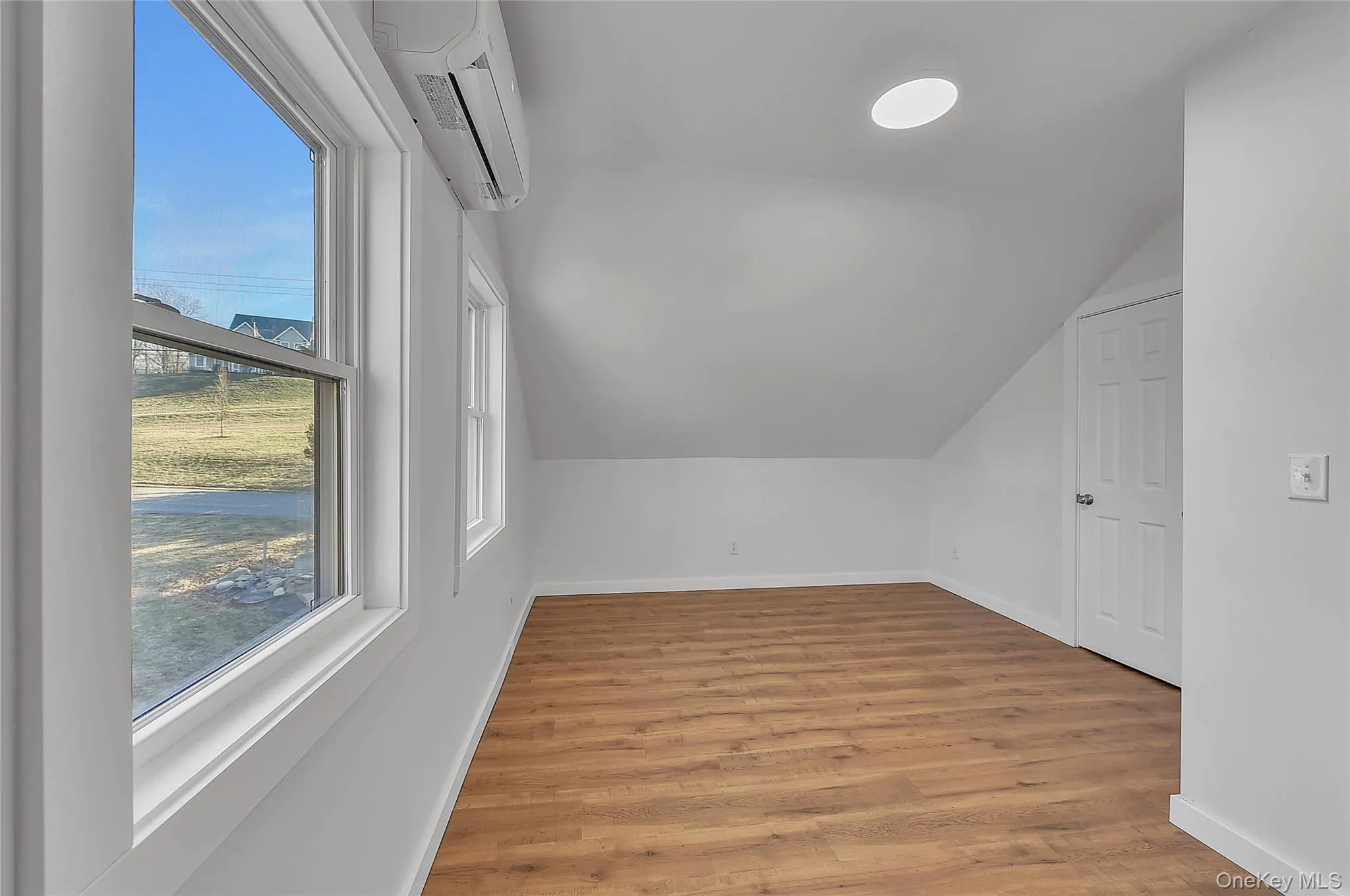 Additional living space featuring a wall mounted air conditioner, light wood-type flooring, and vaulted ceiling Additional living space featuring a wall mounted air conditioner, light wood-type flooring, and vaulted ceiling