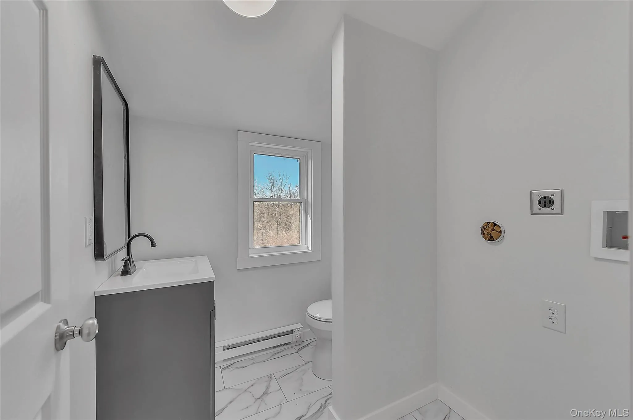 Half bath featuring light marble finish floors, vanity, and a baseboard radiator Half bath featuring light marble finish floors, vanity, and a baseboard radiator