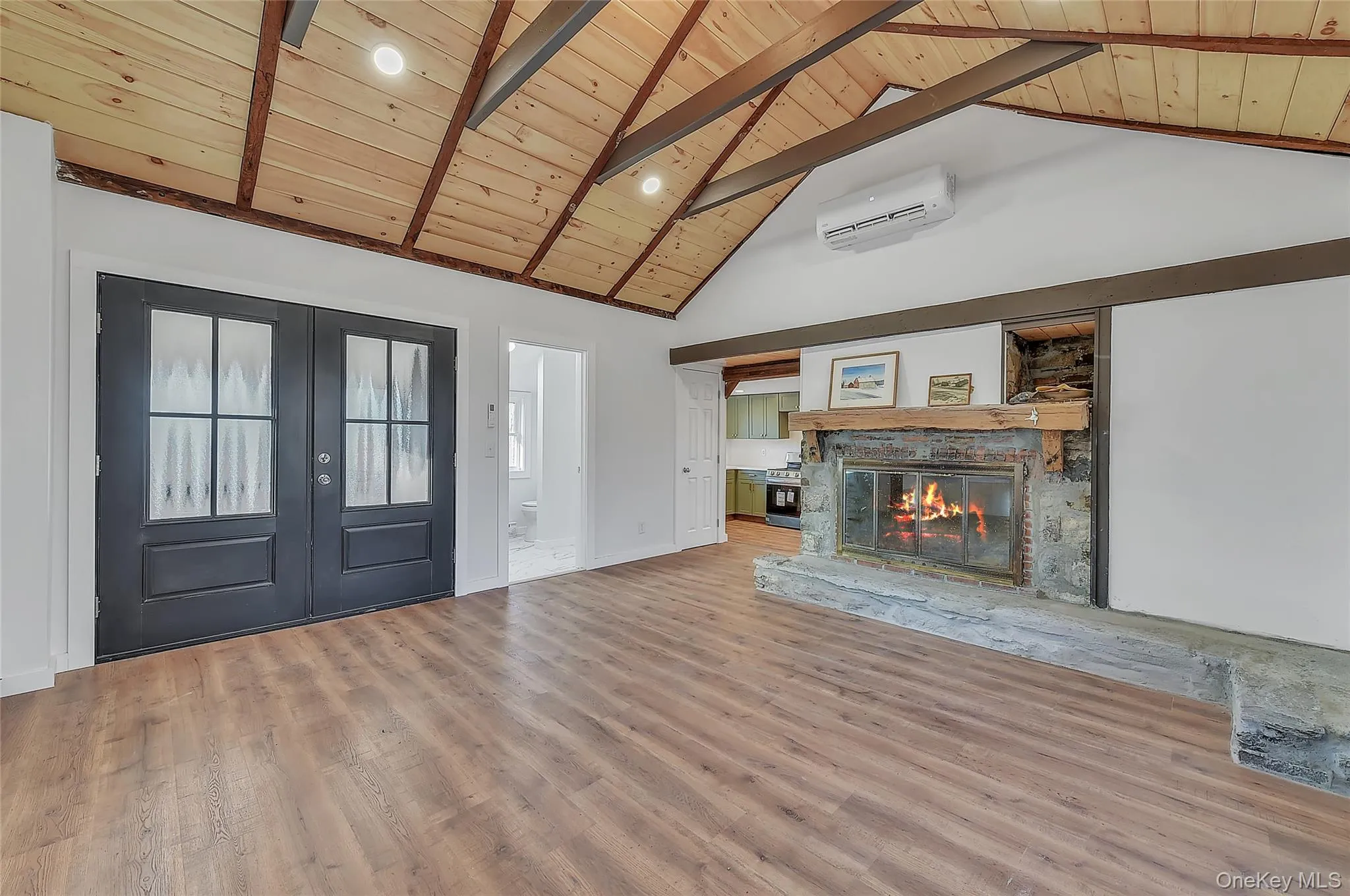 Unfurnished living room with french doors, a wooden ceiling with exposed beams, a wall mounted AC, high vaulted ceiling, and a fireplace Unfurnished living room with french doors, a wooden ceiling with exposed beams, a wall mounted AC, high vaulted ceiling, and a fireplace