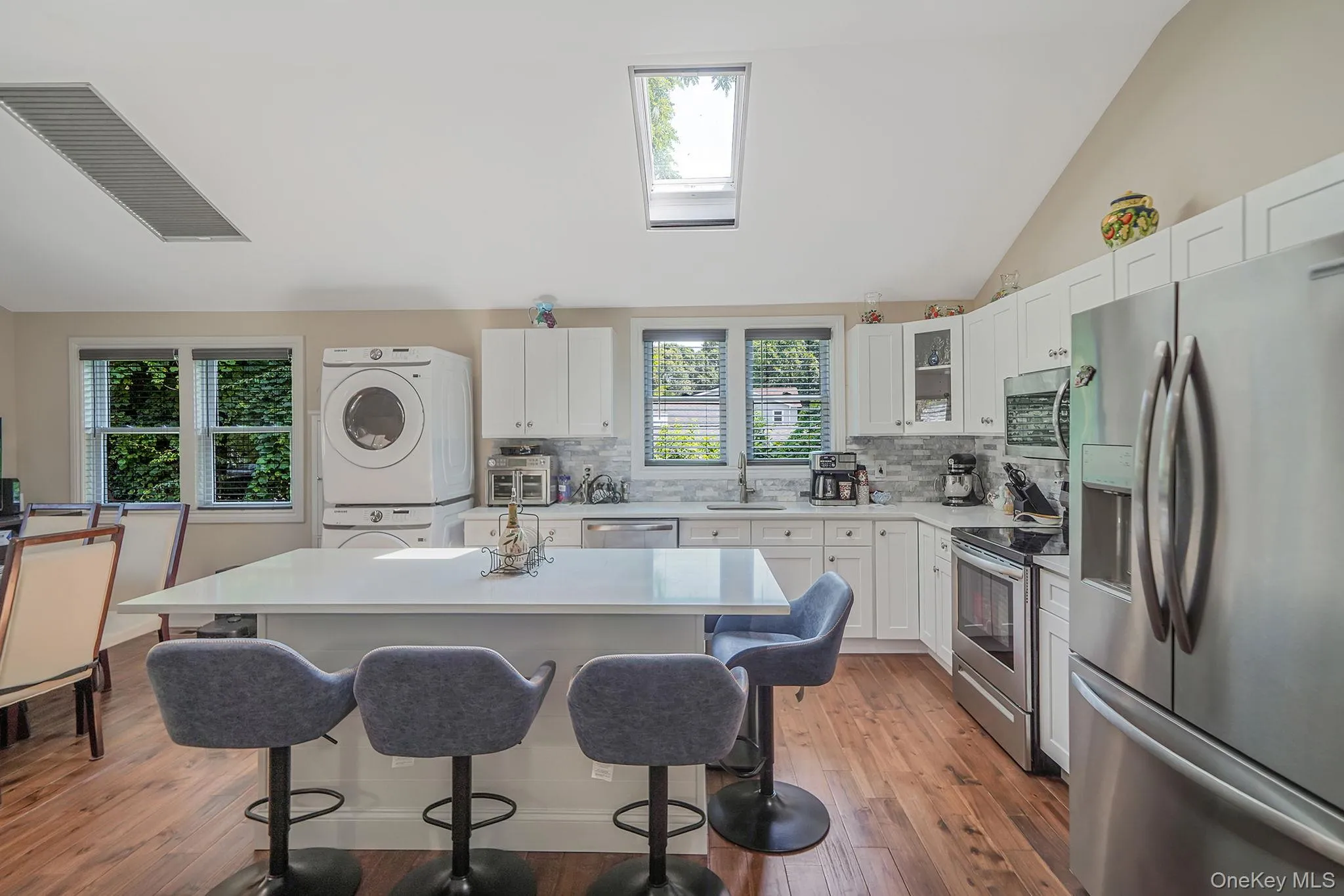 Kitchen with stacked washing machine and dryer, stainless steel appliances, a skylight, a breakfast bar area, and tasteful backsplash Kitchen with stacked washing machine and dryer, stainless steel appliances, a skylight, a breakfast bar area, and tasteful backsplash